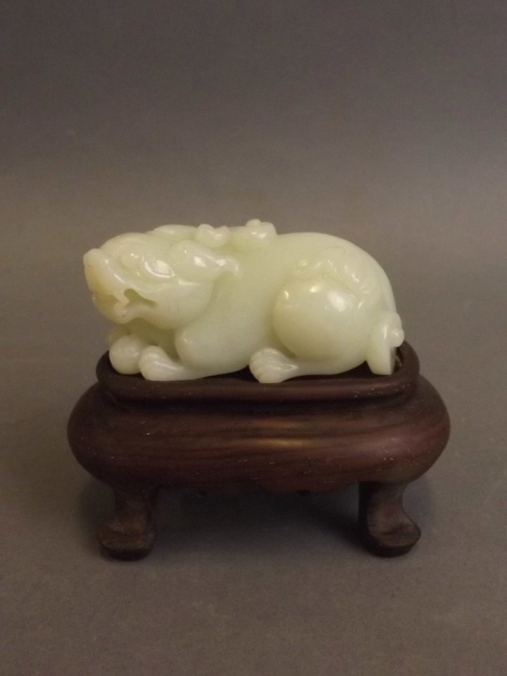 A Chinese celadon carved jade ornament in the form of: A Chinese celadon carved jade ornament in the form of kylin, on a carved hardwood stand, jade 2½" long