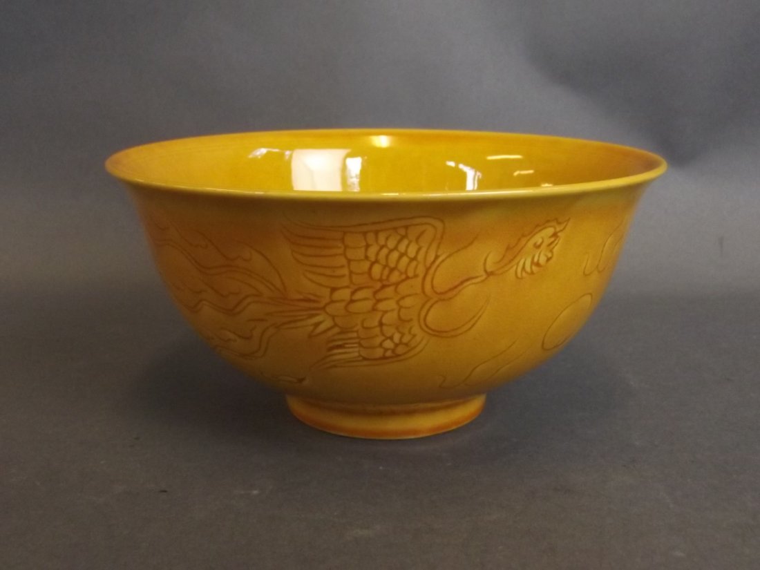 A Chinese mustard ground porcelain rice bowl with: A Chinese mustard ground porcelain rice bowl with incised dragon and phoenix decoration, 6 character mark to base, 6" diameter