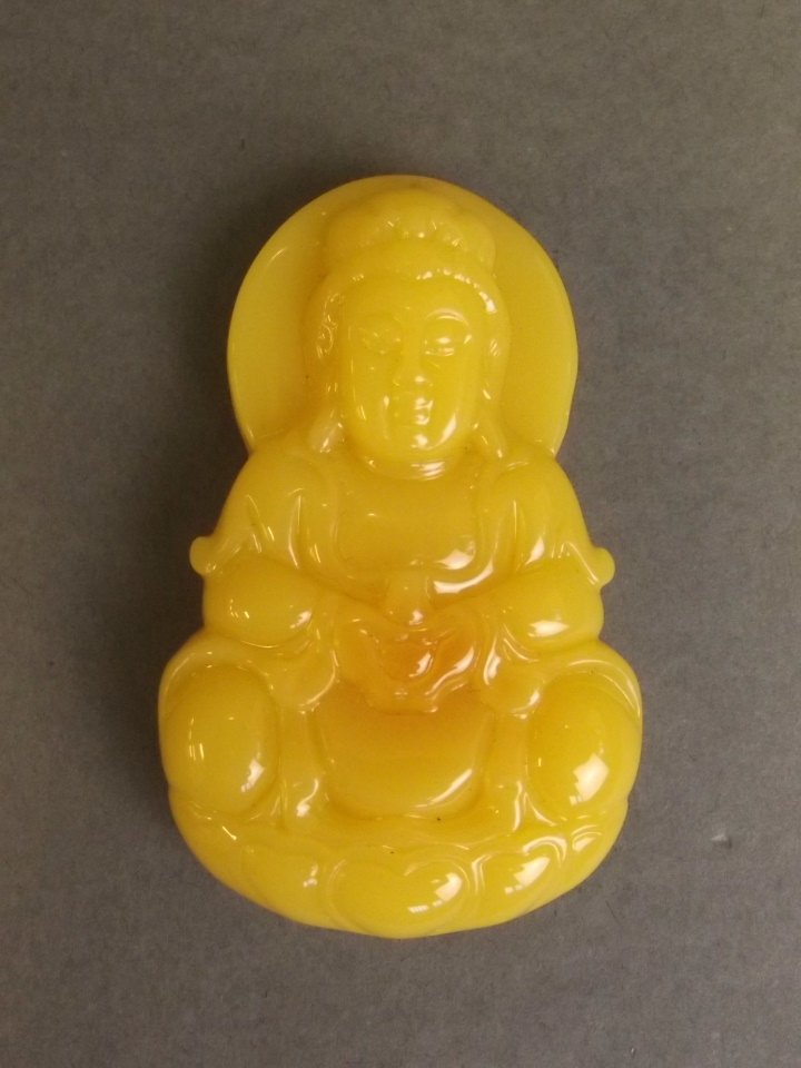 A Chinese amber coloured pendant carved in the form of: A Chinese amber coloured pendant carved in the form of Buddha, 2½" long