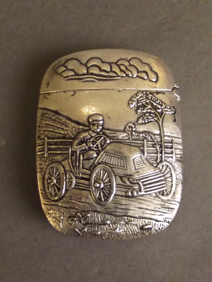 A silver plated vesta case with relief decoration: A silver plated vesta case with relief decoration depicting a gentleman driving a classic car, 2" x 1½"