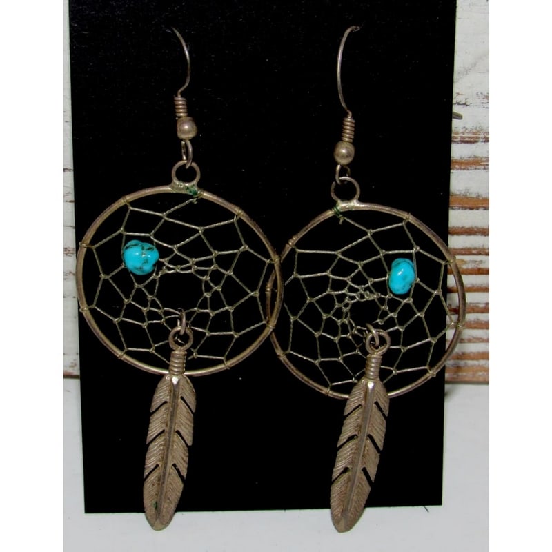 Navajo Sterling Silver Turquoise Dreamcatcher Dangle Earrings: Navajo sterling silver dreamcatcher dangle earrings featuring natural turquoise accents and traditional feather drops. Handcrafted with classic webbed dreamcatcher frames, these earrings symbolize pro