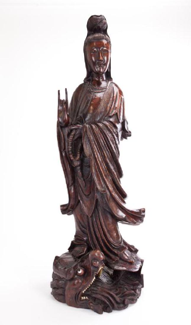 LARGE CHINESE CARVED WOOD STANDING GUANYIN: Carved of a slender form, she wears a flowing robe and has her right hand in Karana mudra. She holds prayer beads in her left hand and stands atop a lily pad base on a dragon's head. H: 36 in.