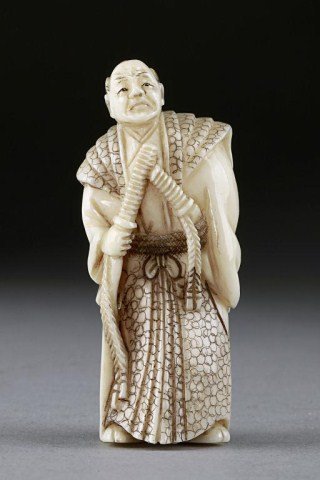 IVORY NETSUKE FIGURE OF A WARRIOR: He holds a long samurai sword in his right hand, and a knife tucked in his belt on the left. Artists signature on the base. H: 2 1/8 in.(5.5cm)