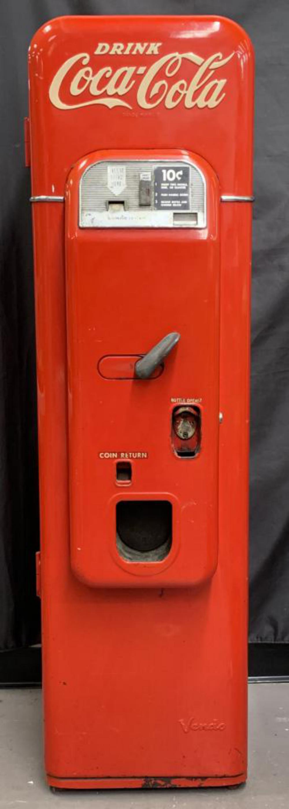 Vendo 44 Coca Cola Bottle Coin Op Vending Machine: Circa 1950's. Vendo 44 Coca Cola Machine. Red and white exterior with hand lettered embossing. Approx. 58" high x 16" wide x 22" deep. Thin design with rear handle and transport wheels. Serial number
