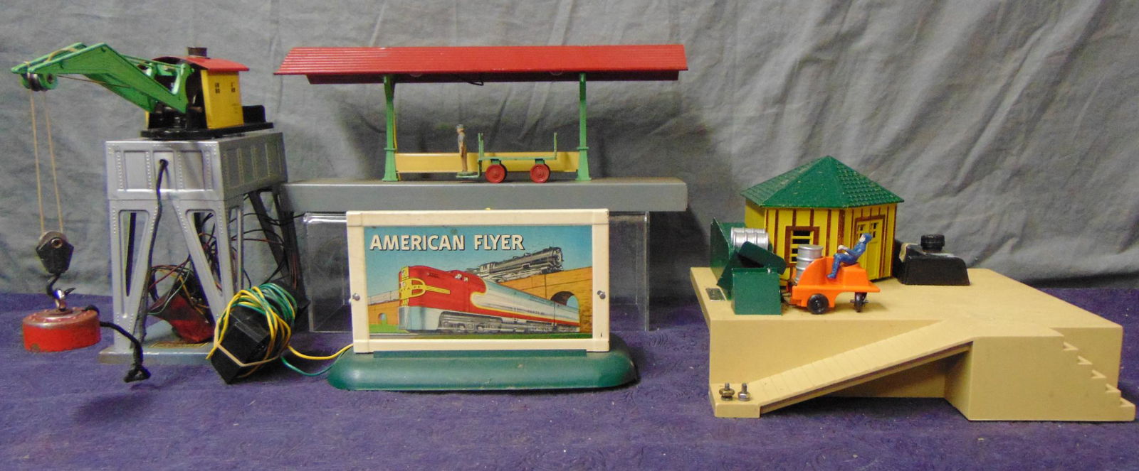 4 American Flyer Accessories: S Ga. Includes a 583 Electromechanical crane; 586K station platform with cart; 779 Oil Drum loader with drums, button and replacement car, steering wheel loose; 23561 Diesel horn billboard with button