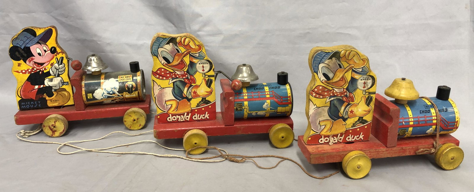 3 Black Label Fisher Price Disney Trains: Includes 2 variations 450 Donald Duck Choo Choo, 9” long; 485 Mickey Mouse Choo Choo. All are paper litho over wood with 450s having original strings. They show some edge wear and signs of playwear.