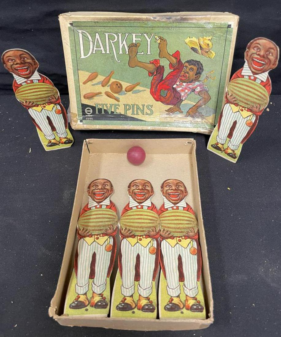 1900 Milton Bradley Darkey 5 Pins Game: #4595. Nice graphics with paper litho in cardboard boys on wood bases with wood ball. Box is a bit warped and has tape residue. Scarce game.
