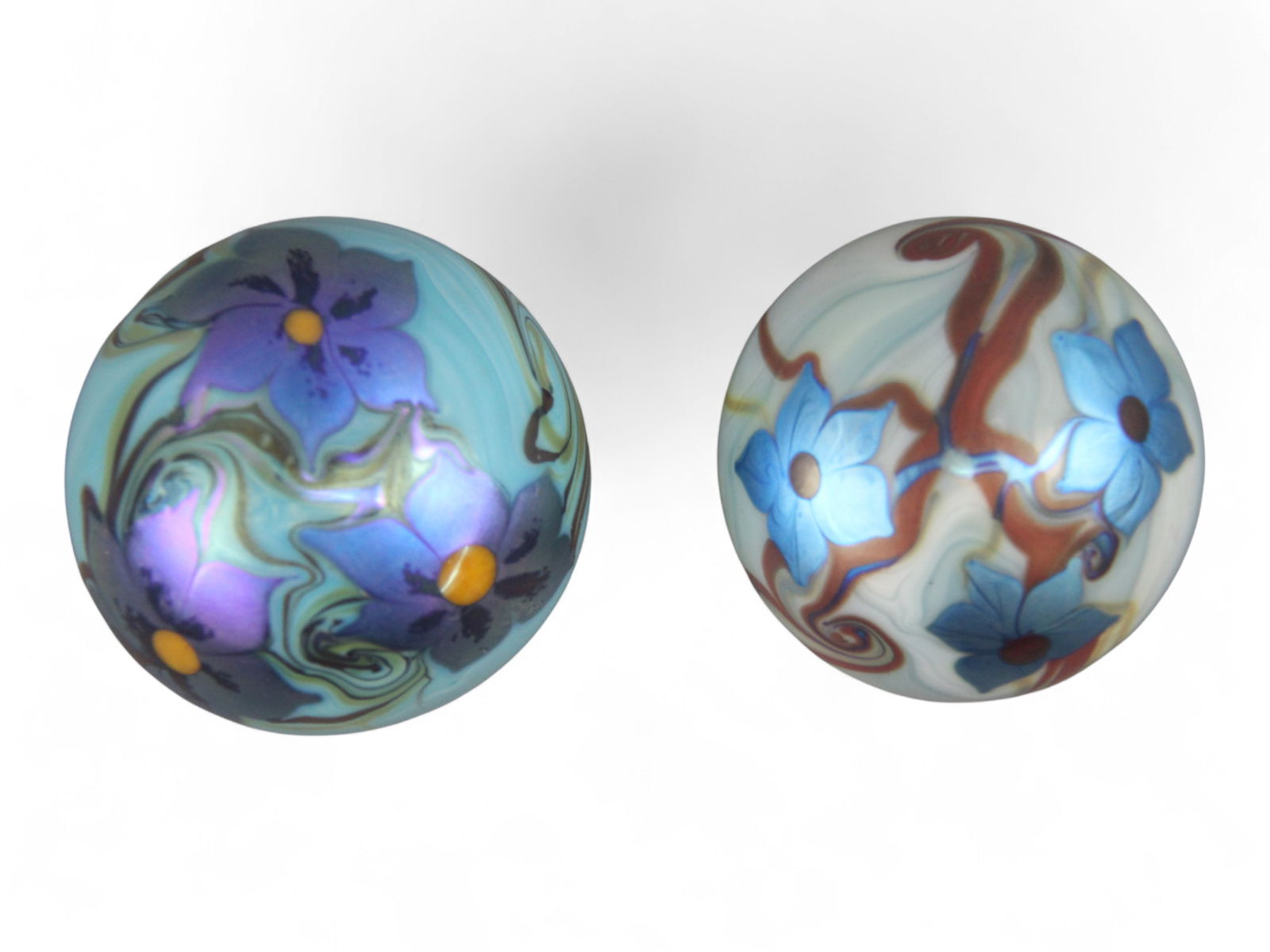 (2) Orient & Flume Floral Art Glass Paperweights: Pair of Orient & Flume hand-blown floral art glass paperweights, each signed on the bottom. One measures approx. 2.5 inches in diameter and features blue blossoms with copper/gold vine accents over a