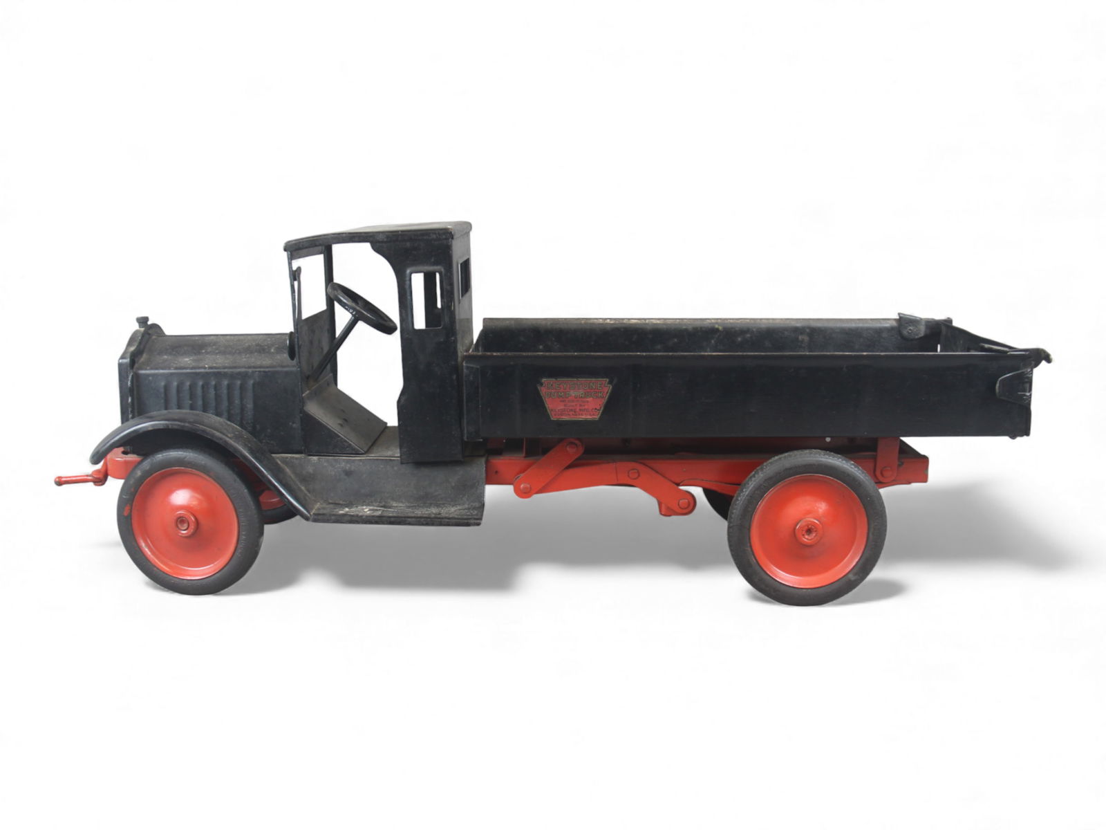 Keystone Packard Hand Crank Dump Truck: Large pressed steel Keystone Packard hand crank dump truck featuring a black cab and dump bed with red chassis and disc wheels. The original decals remains on the bed sides and radiator grille, howeve
