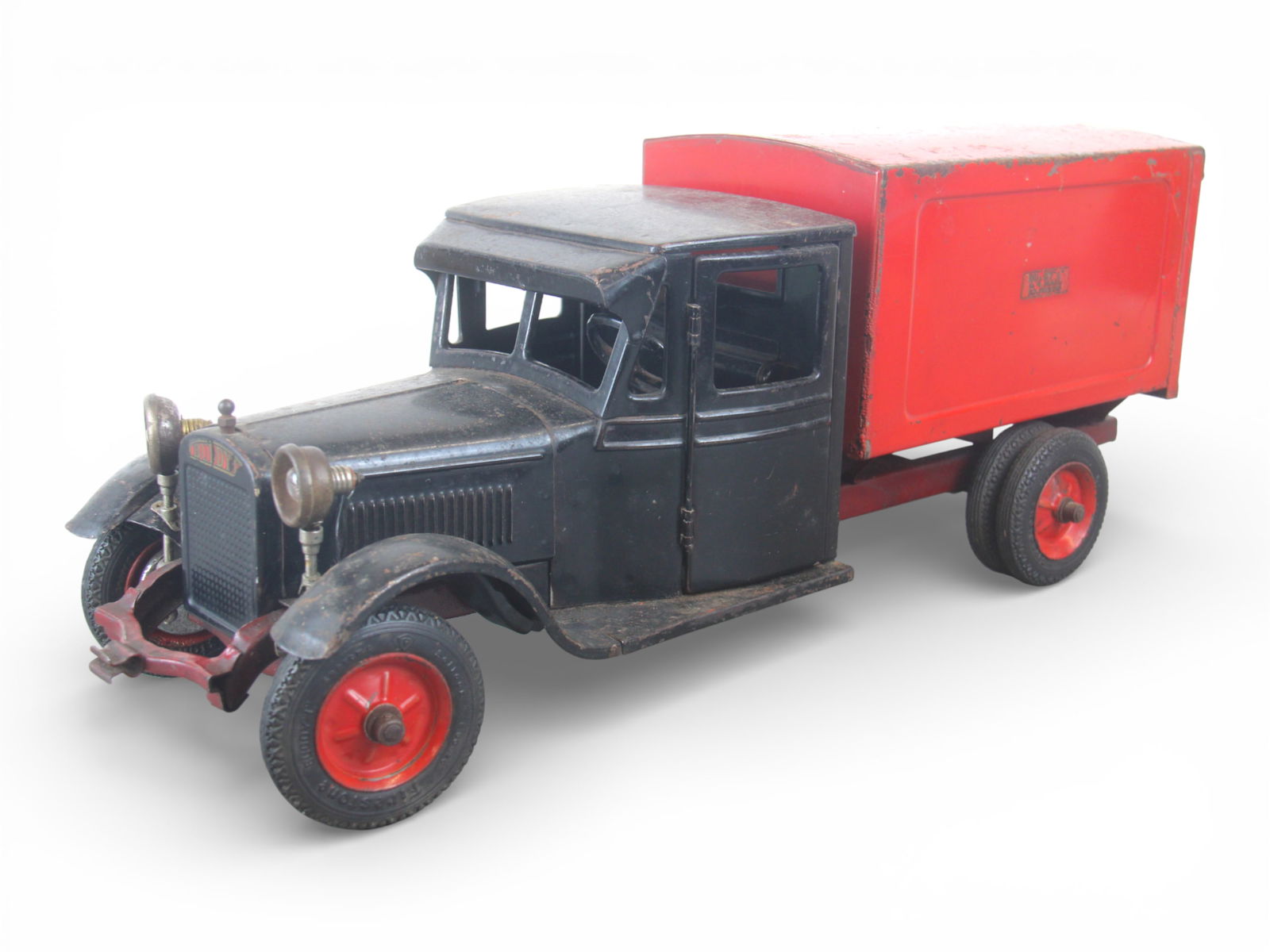 Buddy L Jr Delivery Truck: 1927. Great series pressed steel with rubber tires, 23" long. It is equipped with opening doors, functional steering with tracking electrical headlights, untested. Rear box has its chains, missing