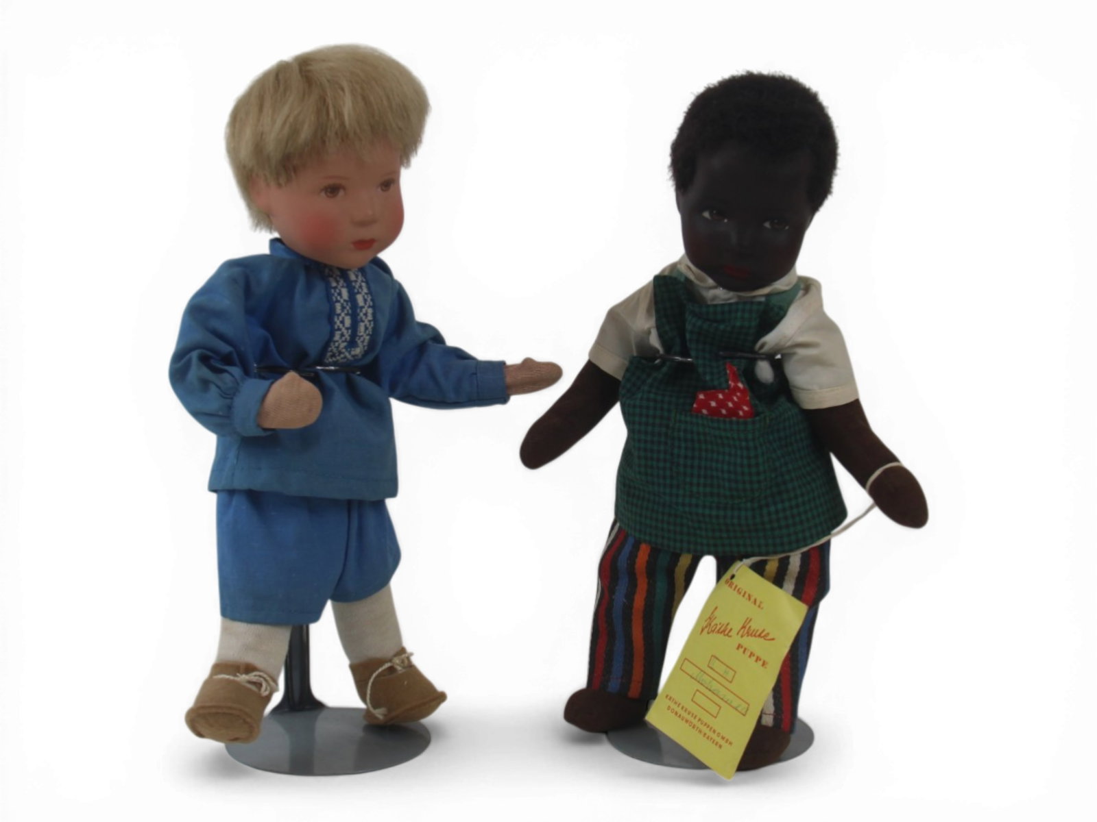 (2) Kathe Kruse Boy Dolls: Two 10 inch Kathe Kruse boys with celluloid heads on wired cloth bodies, including Mohamed black boy doll with tag and a blond boy in original clothes and shoes. Circa 1960s. Shipping: Weiss Auctions 