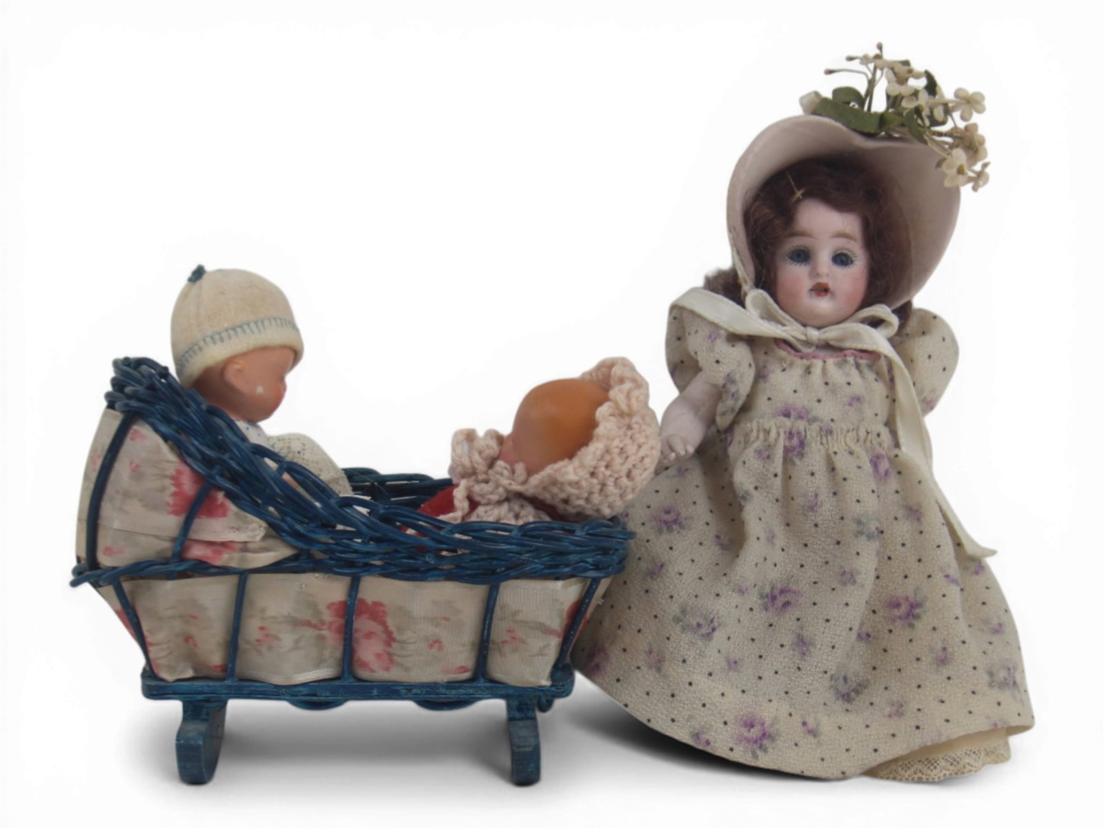 (3) German Dolls in Asian Costume: Group including two small babies in wicker cradle and one 6 inch all bisque girl doll with bonnet and antique dress. Circa 1900. Shipping: Weiss Auctions offers full-service, in-house shipping for nea