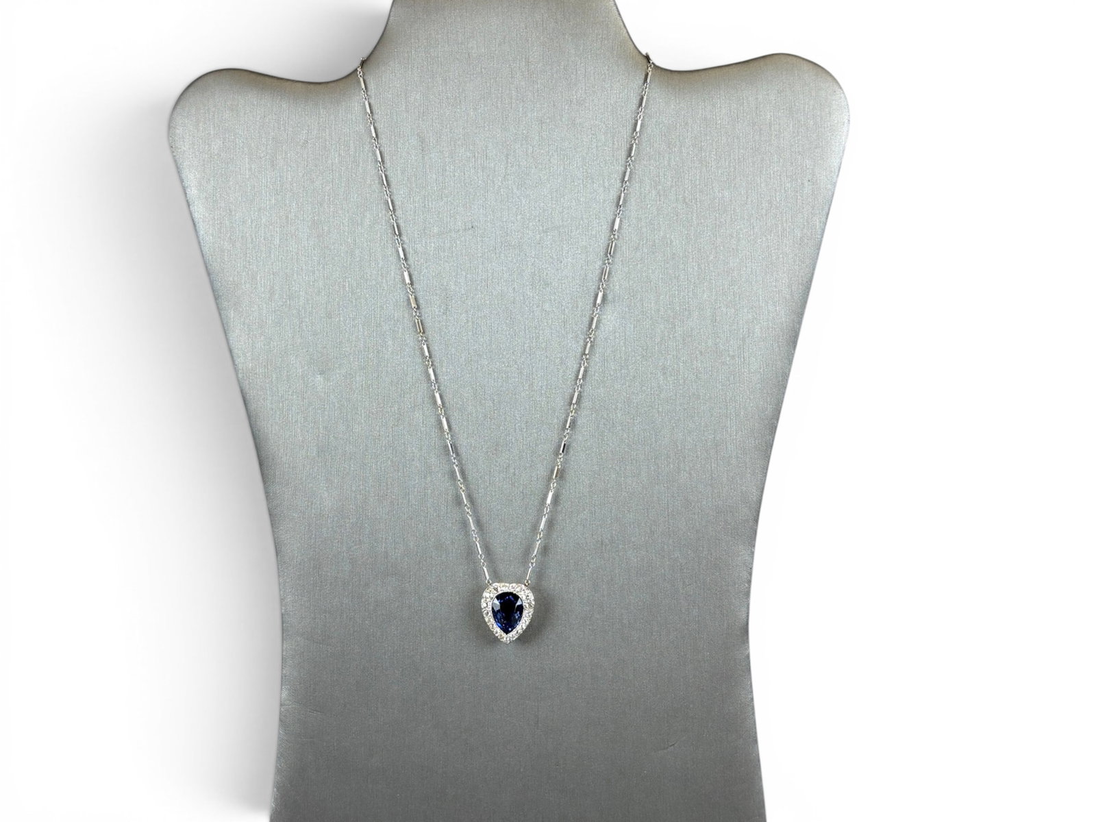14K Gold Sapphire Diamond Necklace: 14K white gold pendant necklace set with a synthetic blue sapphire in pear shape measuring approximately 13.20 x 9.95 x 7.56 millimeters, estimated weight 8.00 carats. Surrounded by a halo of