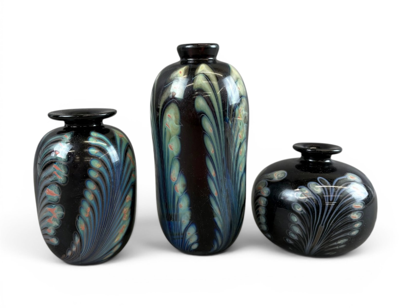 (3) Robert Burch Art Glass Vases: Group of three Robert Burch studio art glass vases, each featuring dark iridescent grounds with stylized feather and pulled floral decoration in blue, green, and opalescent tones. Includes a squat glo