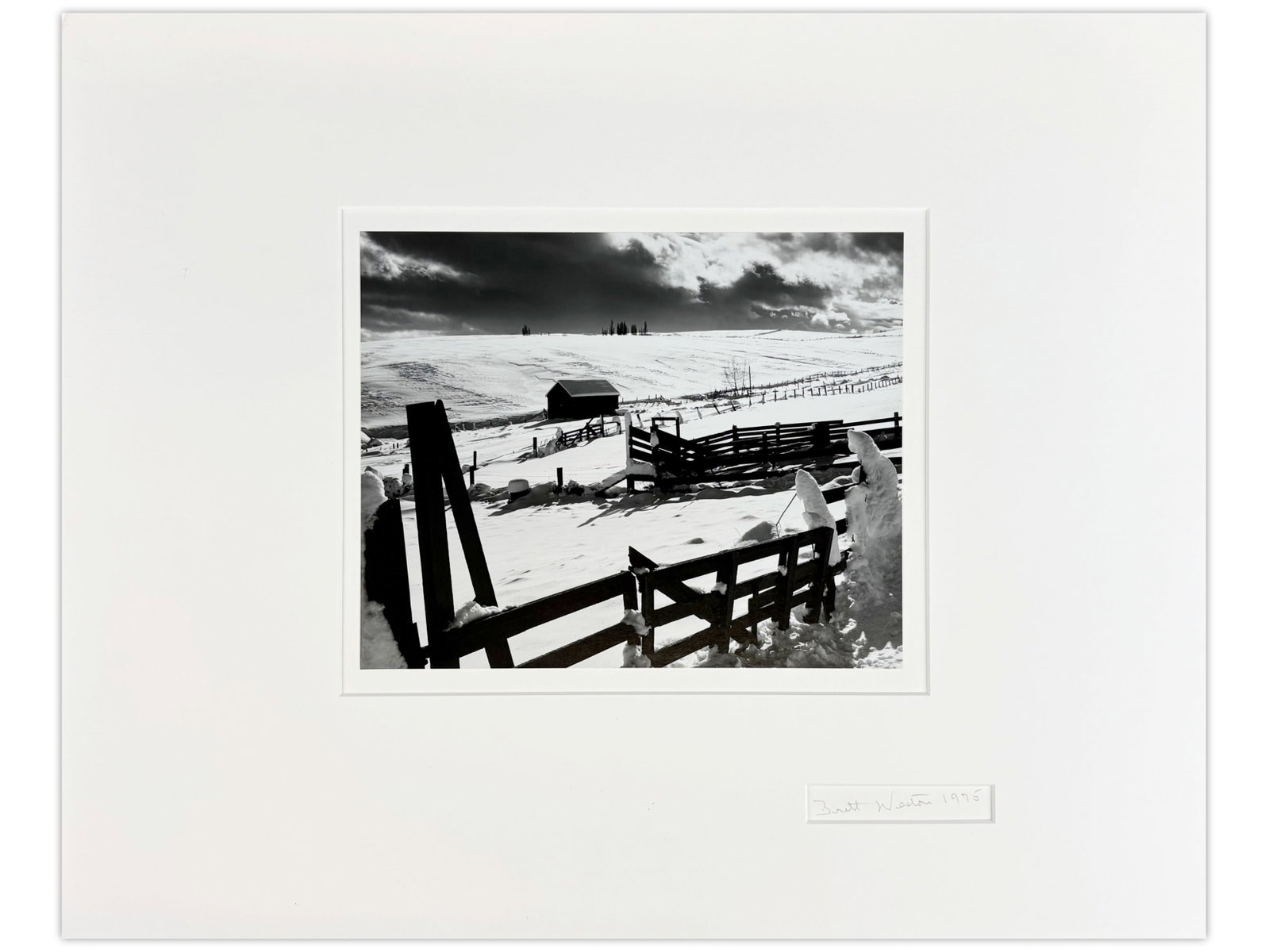 Brett Weston Signed Photo, "Farm in Snow", 1975: Brett Weston (American, 1911-1993). Unframed gelatin silver print, "Farm in Snow", signed and dated 1975 (lower right on mat). Sight seen approx. 9.5" x 7.5". Print is mounted and matted with 16" x