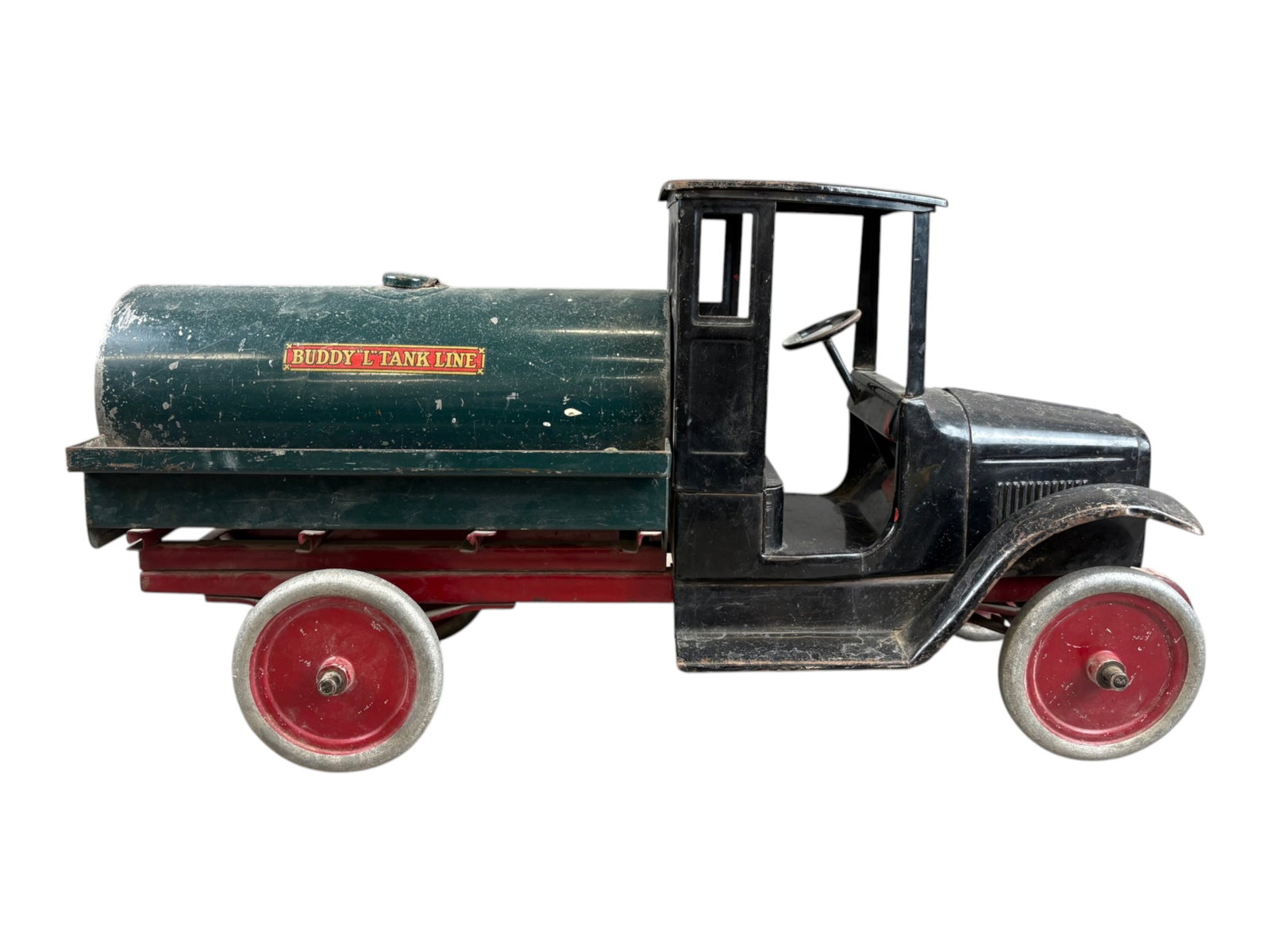 Buddy L Pressed Steel Tank Line Truck: Vintage Buddy L "Tank Line" pressed steel tanker truck. Features a black enclosed cab and hood, dark green cylindrical tank, red chassis, and red steel disc wheels with silver-painted rims. Tank