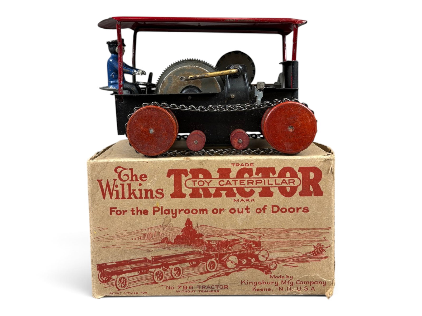 Boxed Wilkins 796 Caterpillar Tractor by Kingsbury: Pressed steel open frame tractor with chain tracks and wooden wheels. Made by Kingsbury Mfg Co. Approx. 8-3/4" long. Includes cast iron driver, and crank mechanism. Shows light playwear with scuffs an