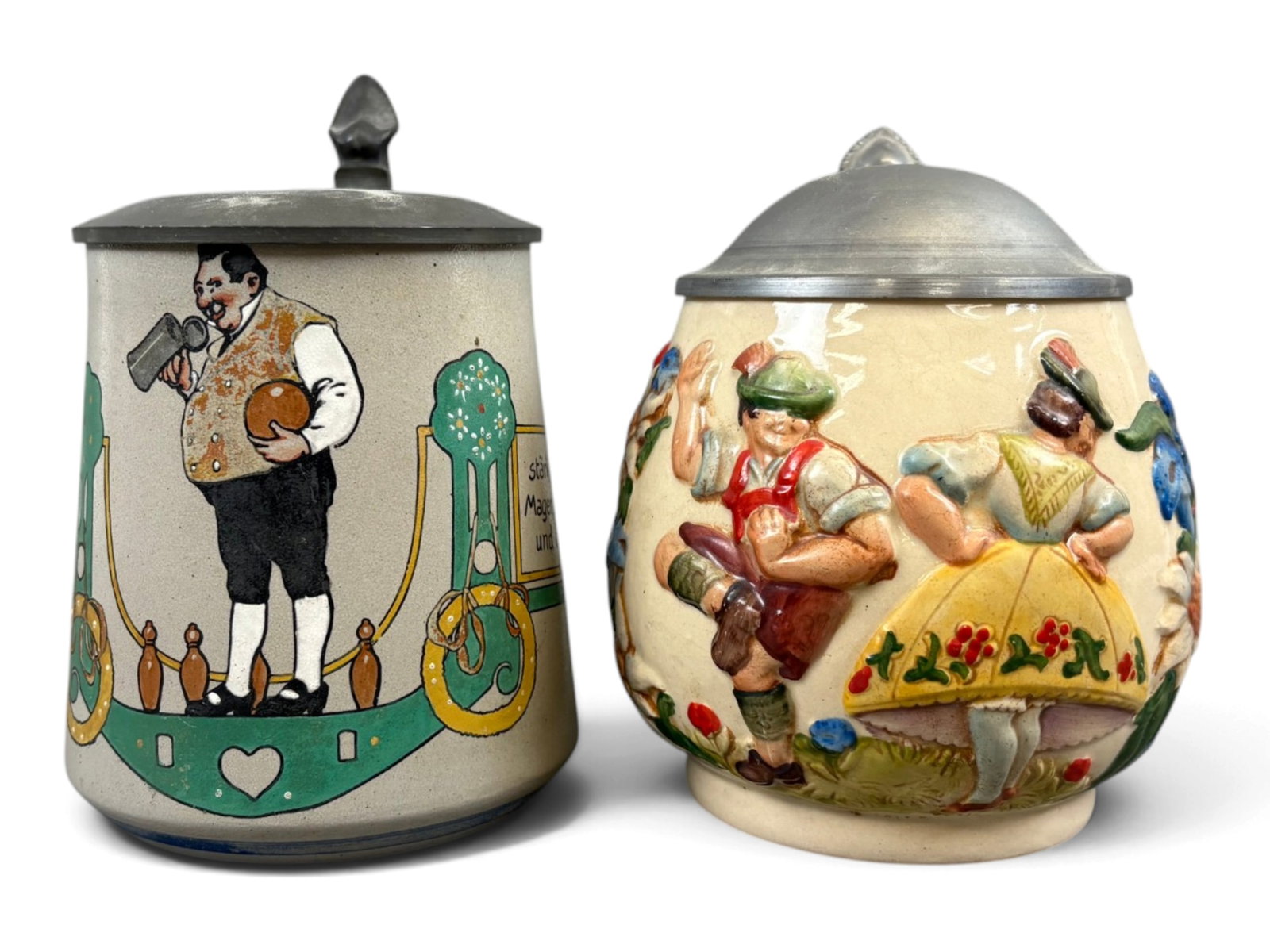 (2) German Bowling & Dancing Beer Steins: Pair of German beer steins, including a stoneware example with a bowling scene, measuring approximately 6 inches tall, and a half-liter stein depicting people dancing, measuring approximately 5-1/2 in