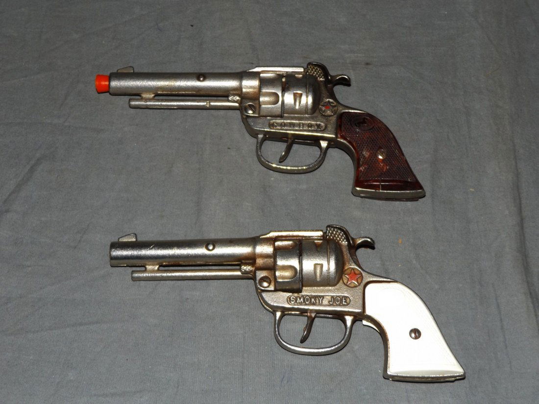 (2) Vintage Hubley Cast Iron Toy Cap Guns: Includes Smoky Joe and Cowboy. Both with plastic grips. The grips on the Cowboy are cracked and small chipped piece from bottom missing. Trigger and hammer are both in working condition. Examine