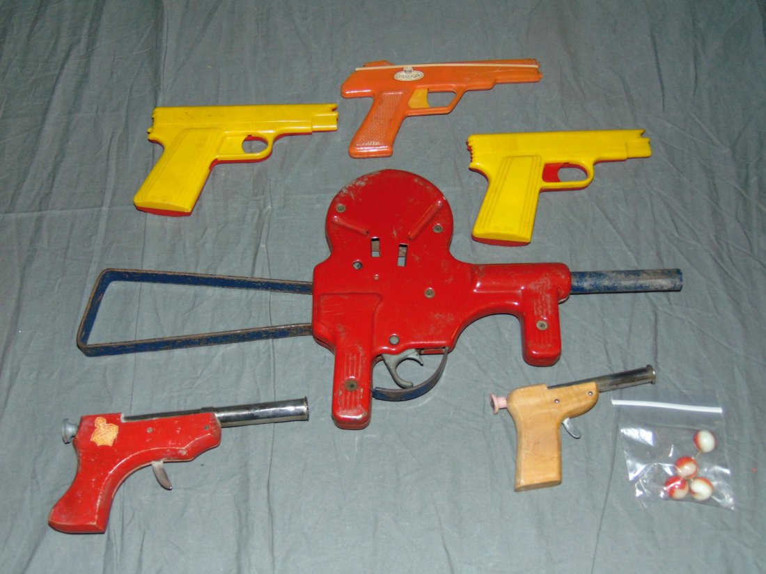 Mixed Lot of Toy Guns: Includes (3) plastic rubber band guns, (2) pencil shooter guns, and 1930's cork ball gun. Each shows some wear. Plastic rubber band guns have some small chips and cracks.