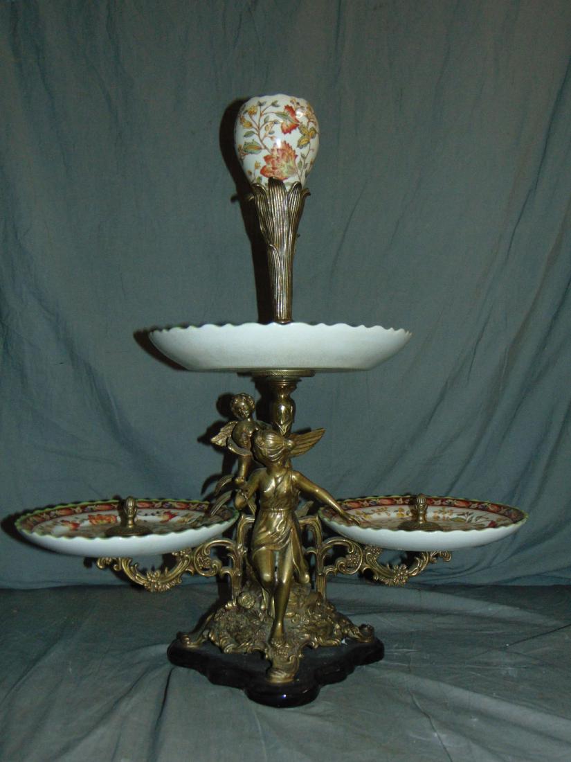 Bronze and Porcelain Multi Tiered Epergne: Approx. 26" tall. Features 3 porcelain tiers and porcelain centerpiece. Some crazing to the porcelain pieces. Features Bronze woman figure with putti. Shows some wear. Examine.