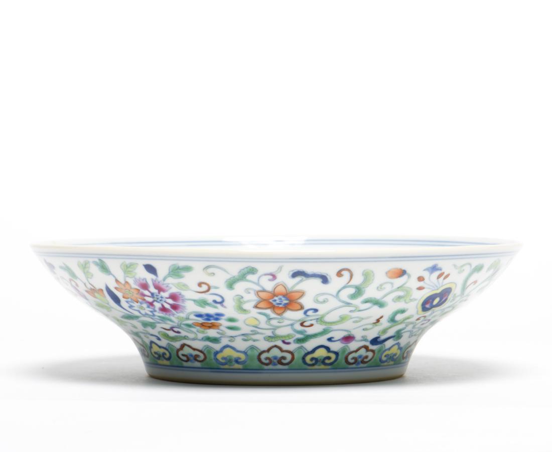 A Doucai Anbaxian Ogee Lotus Dish: The central medallion decorated with a flower-head surrounded by four peaches interspersed with stylized lotus scrolls, the rounded flaring rim with the Eight Daoist Emblems, anbaxian, each tied to fl