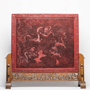 A Cinnabar Lacquered Table Screen
: The plaque finely carved with three ferocious dragons striding amidst flames and clouds in pursuit of the flaming pearl above crashing waves, all reserved on a riding geometric waves, mounted in hardw