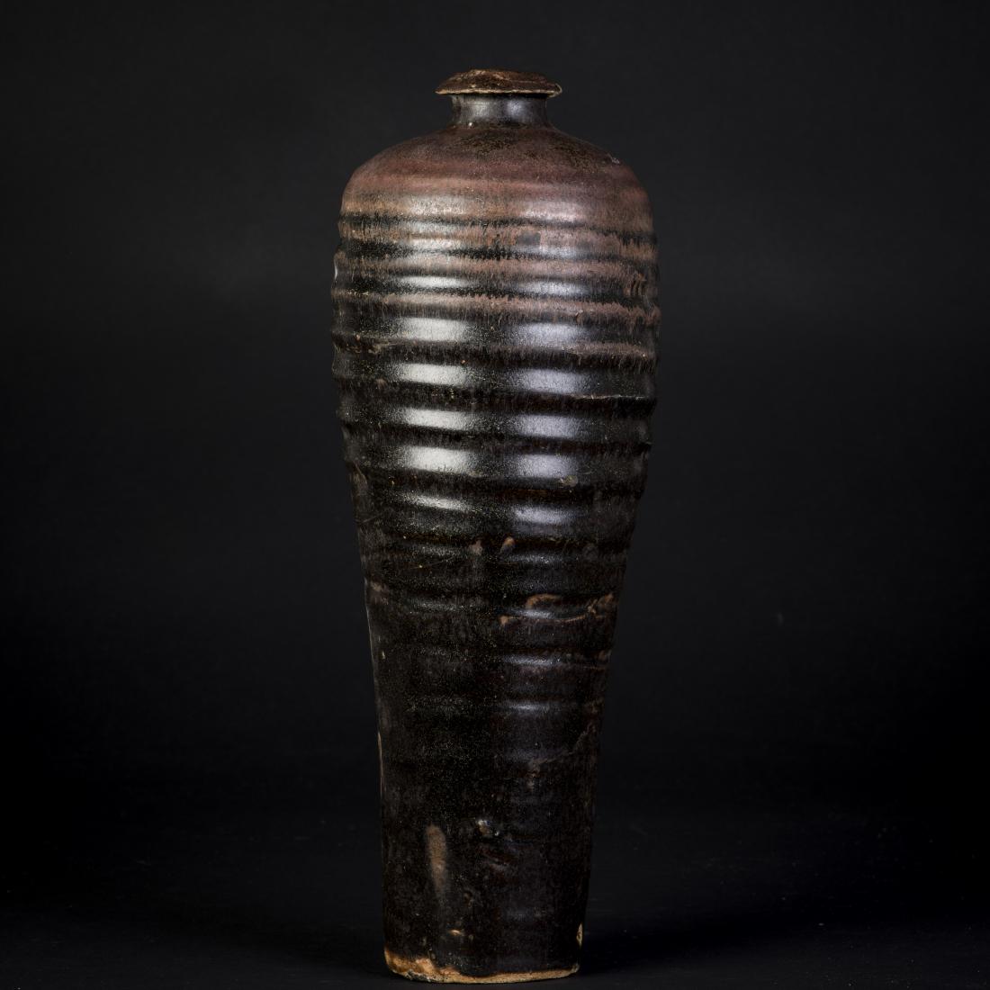A BROWN AND BLACK-GLAZED VASE, MEIPING: The ovoid body with rounded shoulder, short waisted neck and everted mouth, all under an brown-black glaze with black streaks showing over the horizontal bands, base chip in its making. Height 13'' Di
