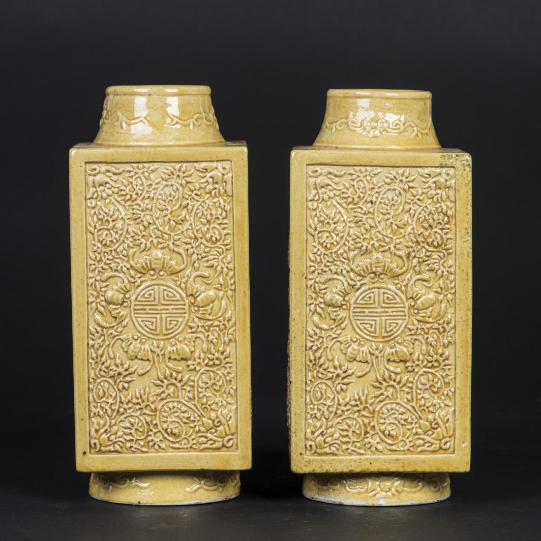 A PAIR OF YELLOW GLAZED SQUARE-SECTIONED VASES: Each molded in relief with five bats encircling a Shou medallion amidst leaf scrolls on each rectangular wall, a flower head and leaf scroll pattern extending around the tapered neck and flared foot, 
