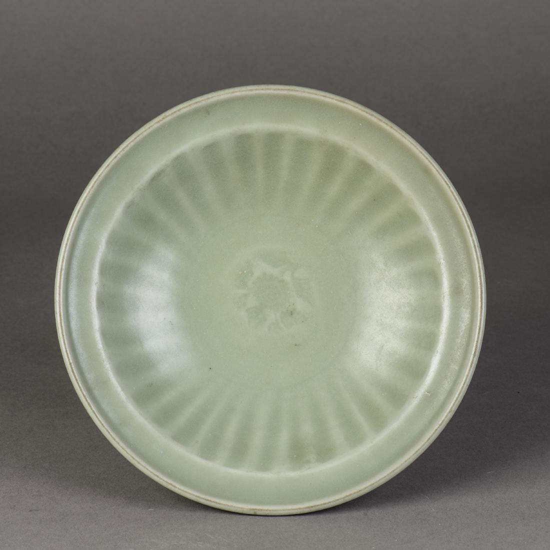 A LONGQUAN CELADON DISH: The dish is decorated with a central moulded floral spray surrounded by deep ribs to the cavetto. It is covered overall in an olive-green glaze which thins and thickens at the decorative designs. Heig