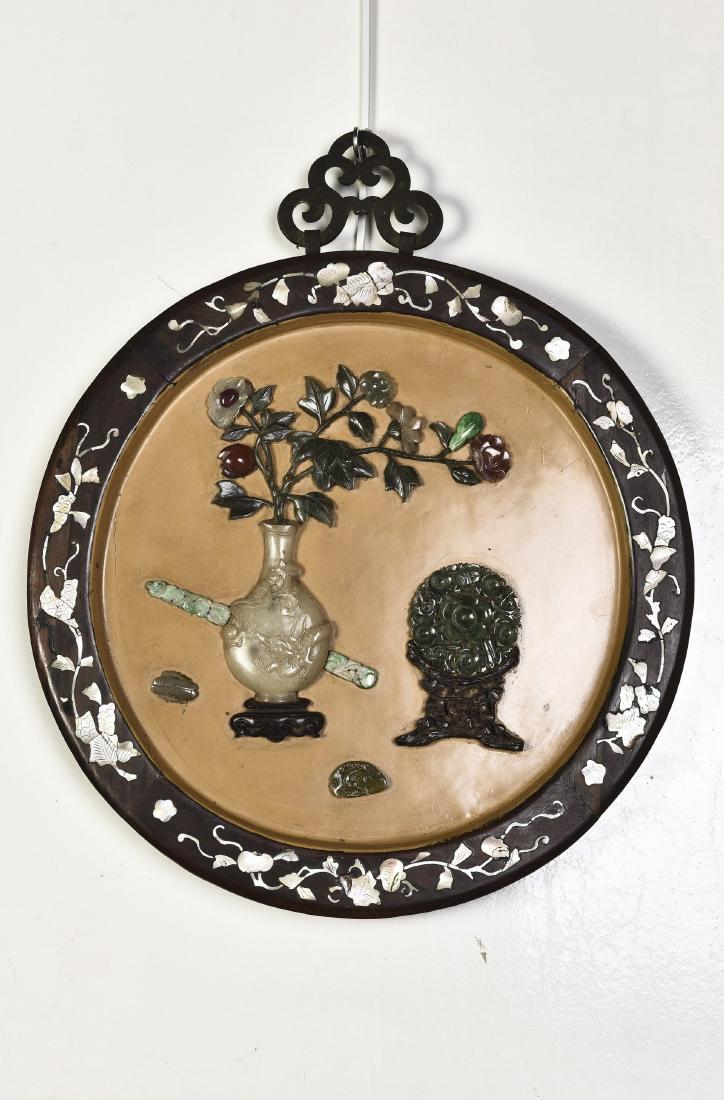 A CIRCULAR SCREEN INLAID WITH JADE, QING DYNASTY: A circular screen inlaid with jade, of Qing period, depicting studio blossoms on vase, ruyi scepter and jade. Diameter 13.75 in. (34.9 cm.)