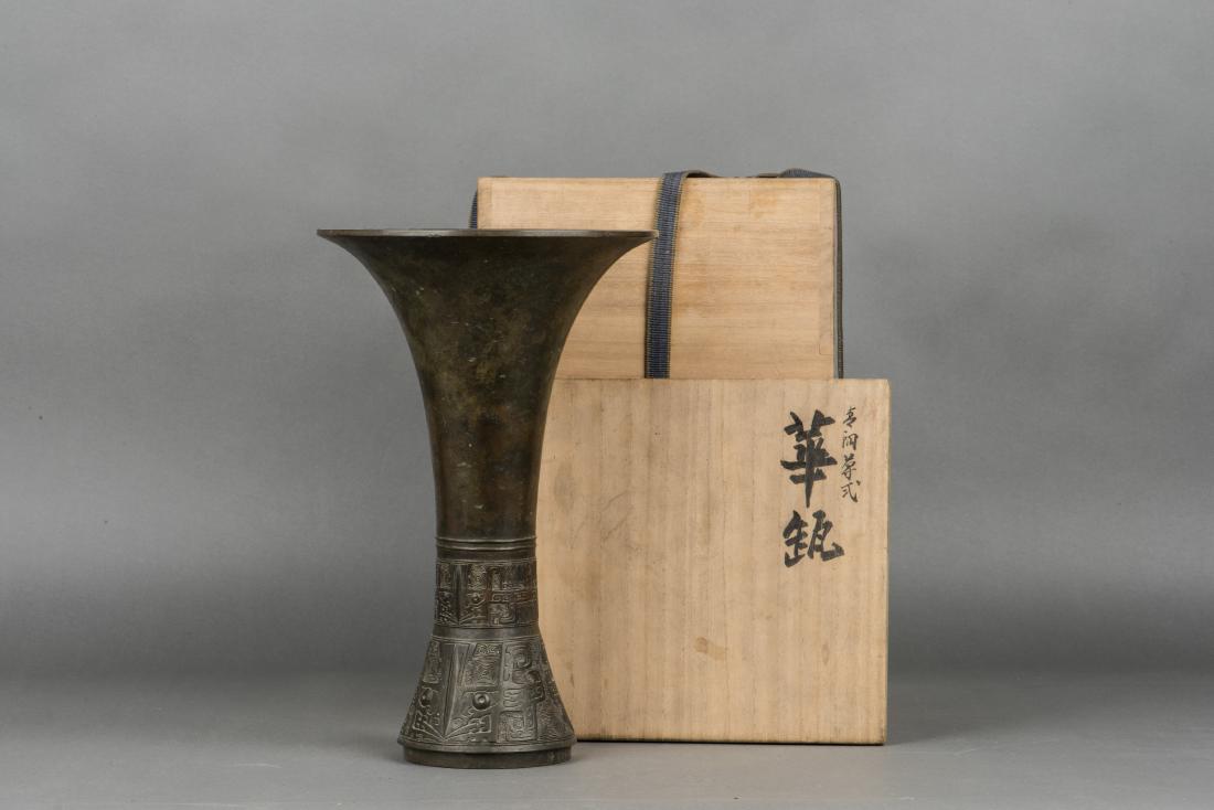 A BRONZE BEAKER VASE, 20TH CENTURY: The beaker vase of archaistic form with a gently spreading foot and flared rim. The middle section and spreading foot with decorative carvings. With a Japanese wood box. Height 30cm Width 19.5cm