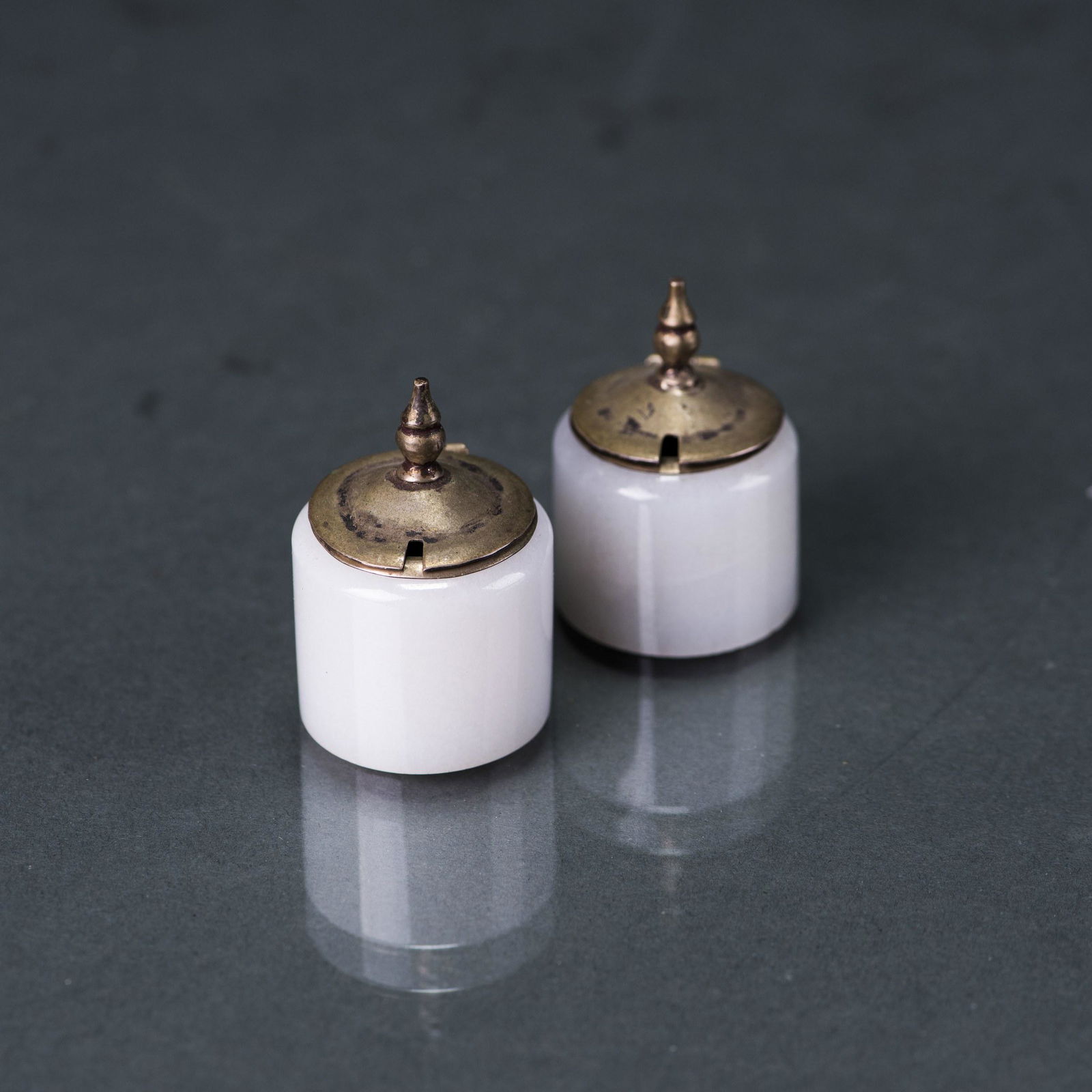 A PAIR OF WHITE JADE COVERED SILVER CONTAINNERS: A pair of white jade covered silver containers, each of a cylindrical form, the outside white jade thumb ring and the silver container is separable. H5.5 x 3.5 cm (2)