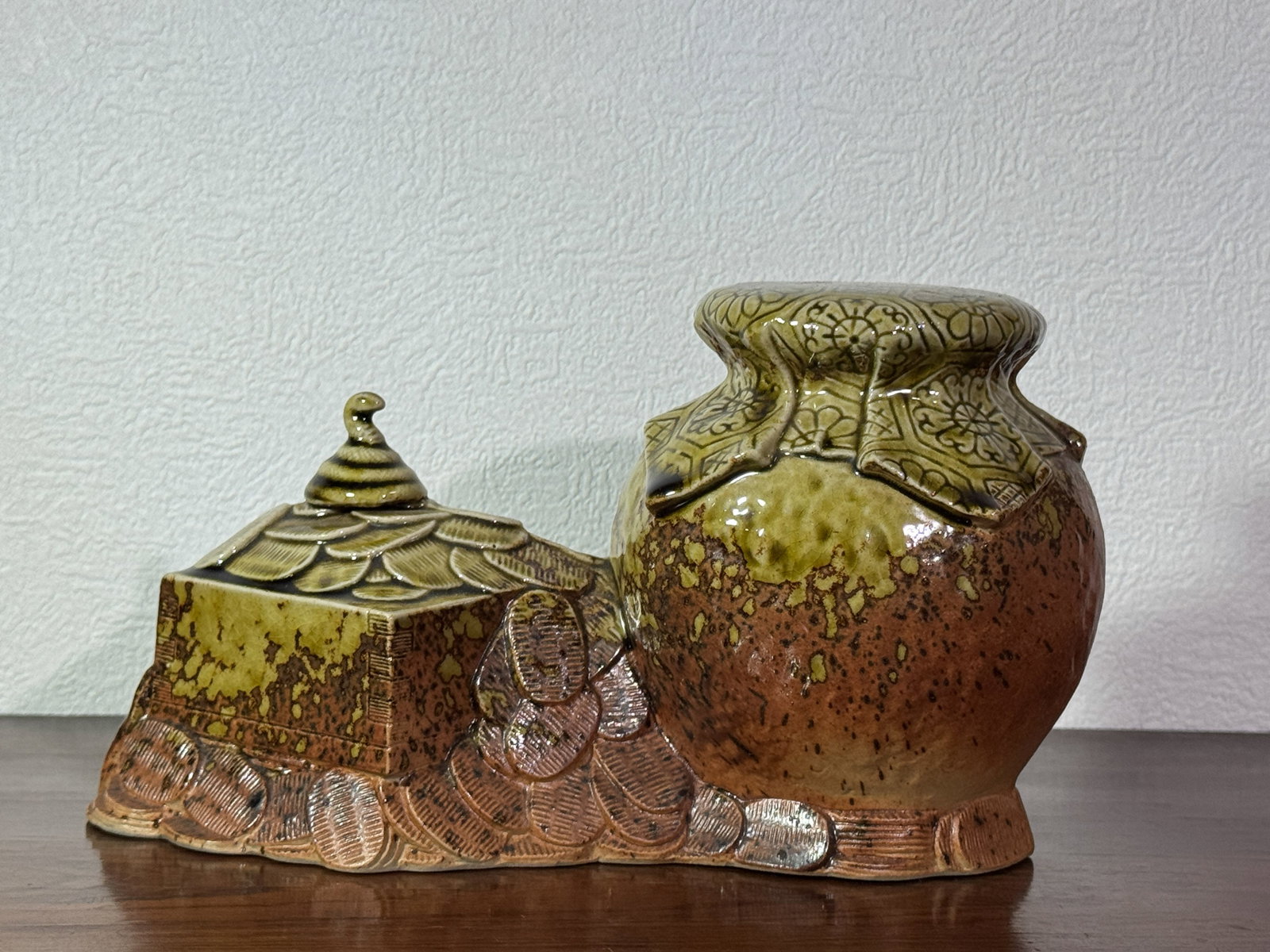 JAPANESE PORCELAIN OKIMONO OF TREASURE COIN STACKS: Japanese porceain okimono of treasure jar with coin stacked on side, guarded with snake at top of coin pile. Dimensions: Length: 9.5 in. (24.1 cm); Height: 5.75 in. (14.6 cm) Note: This item is in New