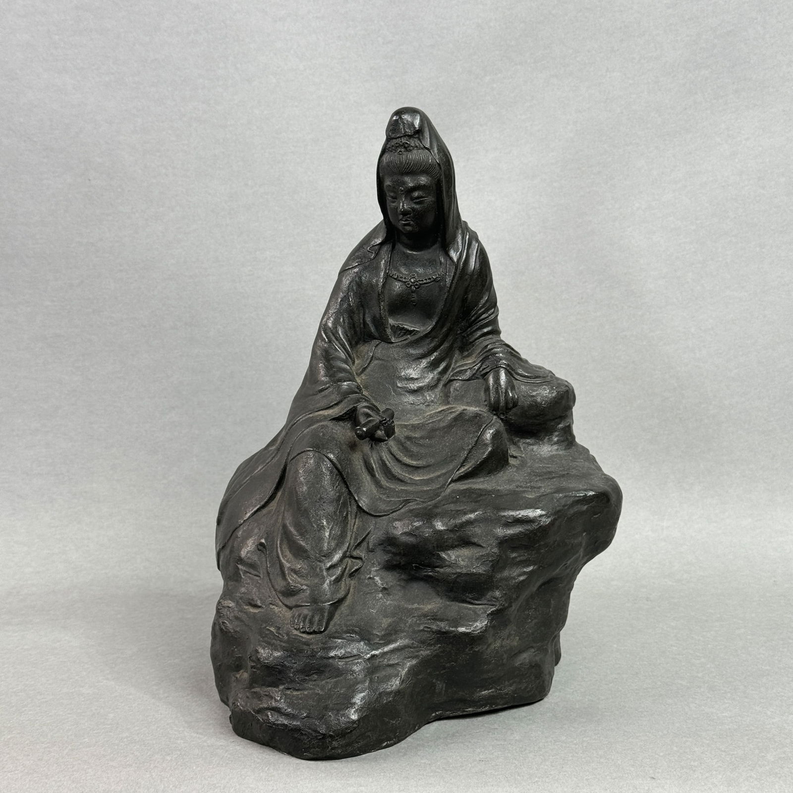A JAPANESE MEIJI BRONZE SEATED KUANYIN: A Japanese Meiji bronze seated Kuanyin, Meiji period, depicting Kuanyin with a scroll in hand, seated on a rock. Dimensions: Height: 11.5 in. (29.2 cm).