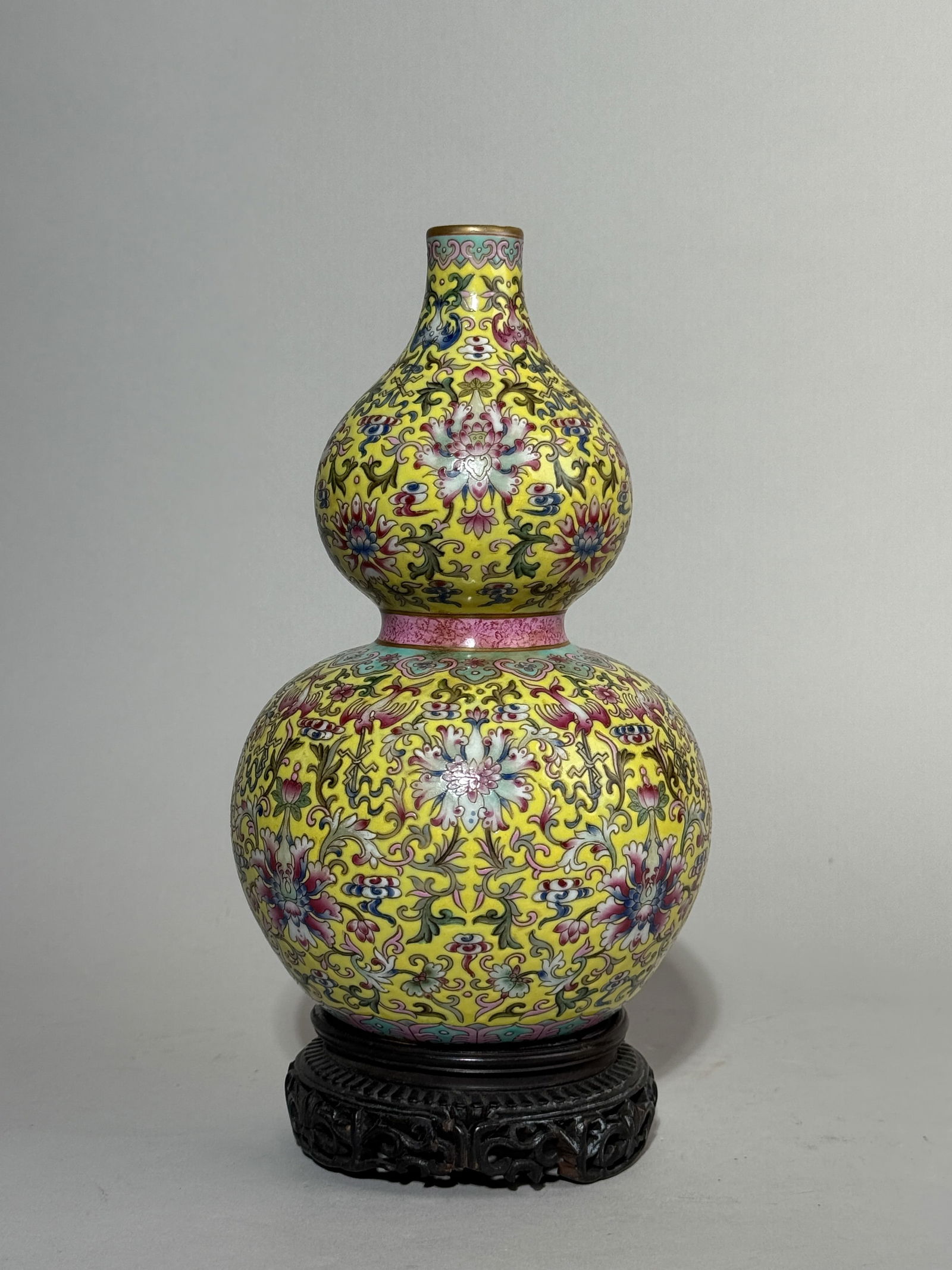 A CHINESE YELLOW-GROUND FAMILLE ROSE DOUBLE GOURD VASE: A Chinese yellow-ground Famille Rose porcelain vase of double gourd shape, decorated with a lotus floral motif, with a hardwood base. Base wood chipped, porcelain in good condition. Dimensions: Height