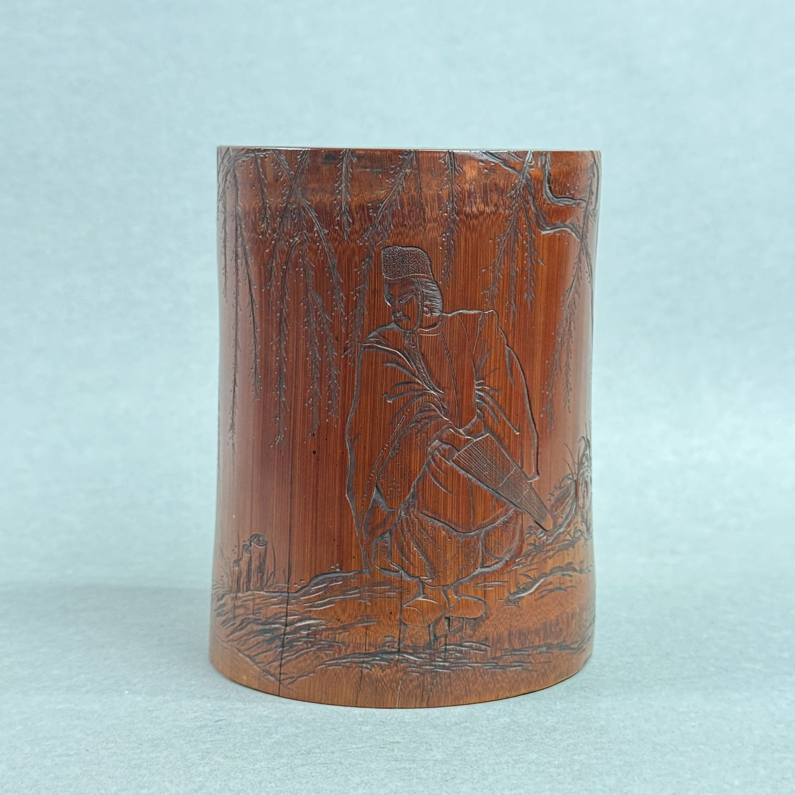 A JAPANESE BAMBOO BRUSHPOT OF PRIEST WITH UMBRELLA: A Japanese carved bamboo brushpot depicting a priest with an umbrella, Edo period, 18th century. Dimensions: Height: 5.25 in. (13.3 cm); Diameter: 4 in. (10.2 cm).