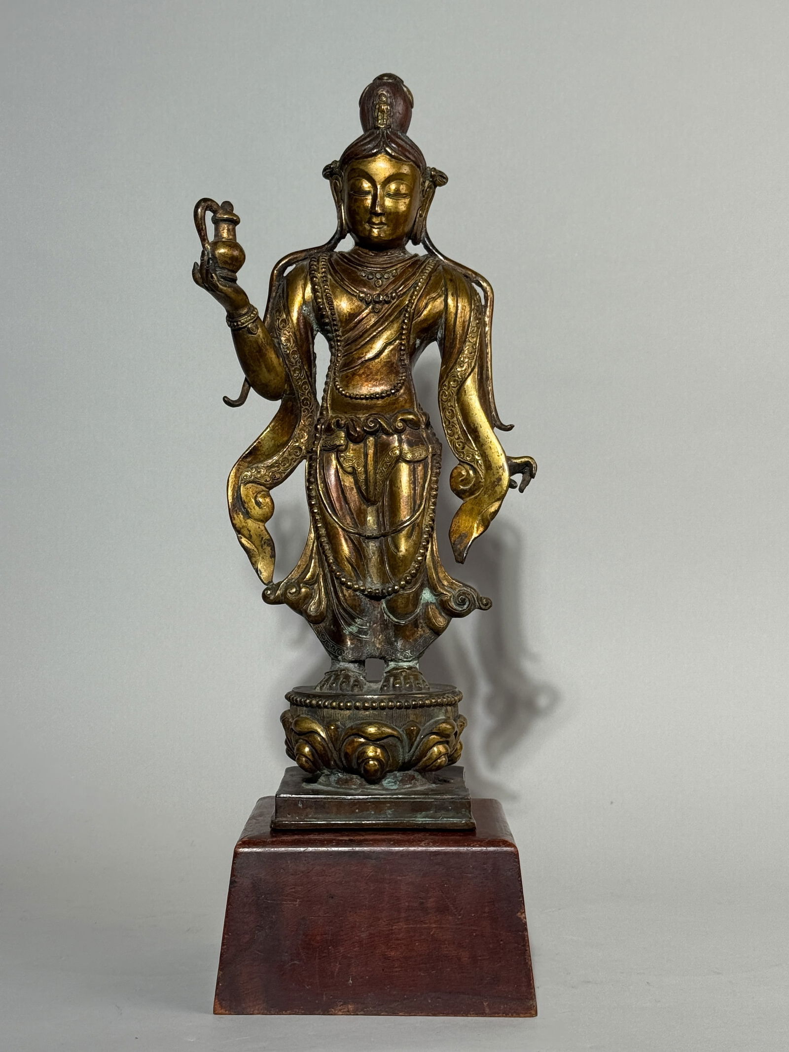 A SINO-TIBETAN GILT BRONZE STANDING TARA: An antique Sino-Tibetan gilt bronze Tara on a hardwood base. Dimensions: Bronze height: 13.5 in. (34.3 cm).