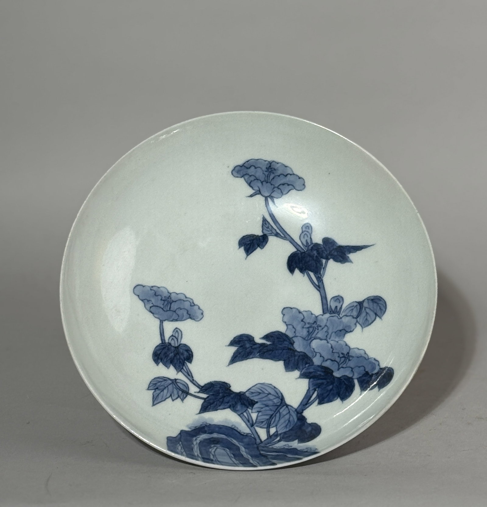 A JAPANESE BLUE AND WHITE NABESHIMA PORCELAIN DISH: A Japanese blue and white Nabeshima porcelain dish with a floral scene, Meiji period. Slightly uneven rim from side view as part of kiln characteristics. Dimensions: Diameter: 8 in. (20.3 cm). Note: