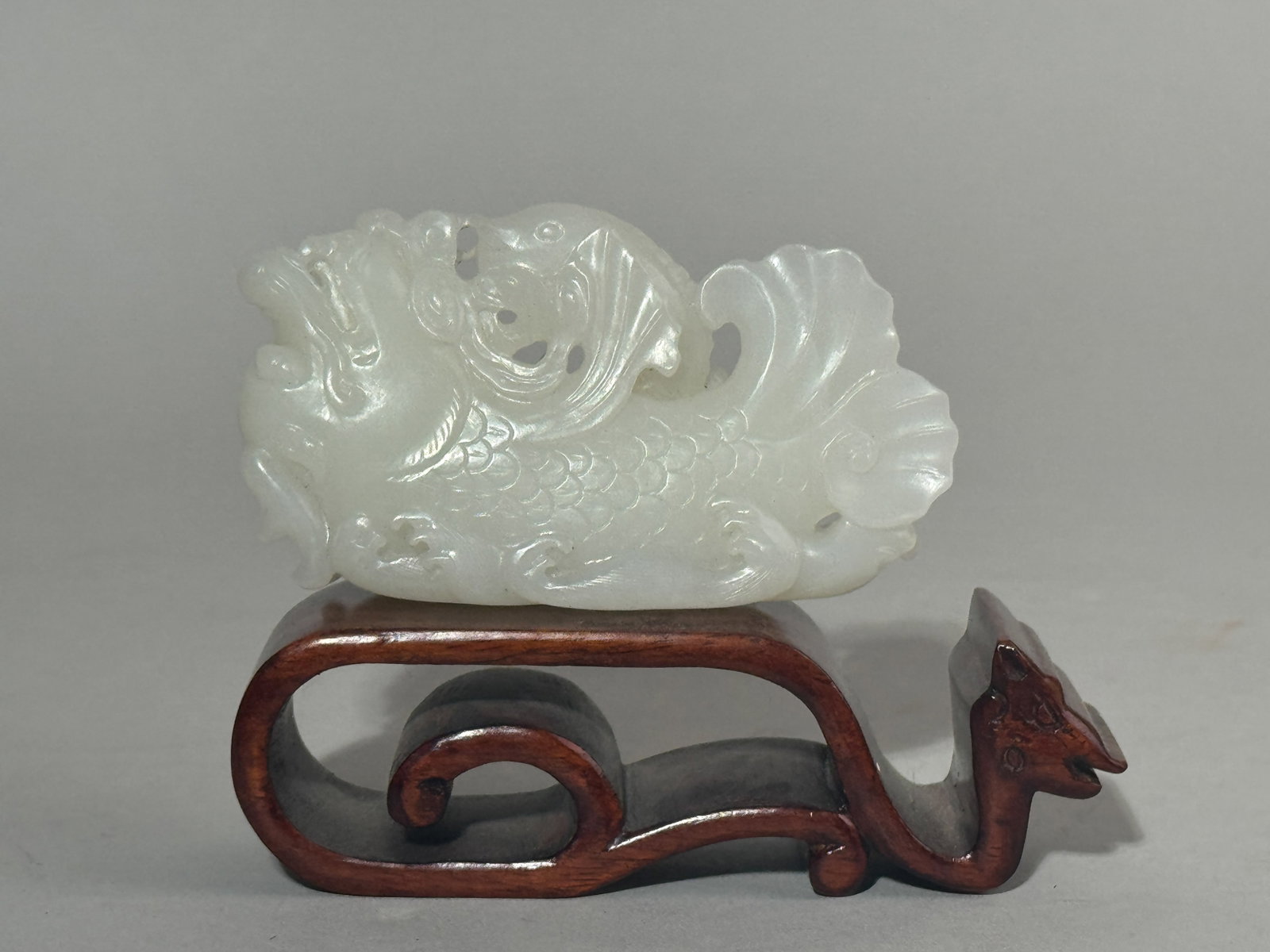 A CHINESE WHITE JADE DRAGON FISH ON SILVER-INLAID WOOD STAND: A Chinese white jade dragon fish on a silver wire-inlaid hardwood stand. Dimensions: Length: 4 in. (10.2 cm). Note: This item is in New York, where it can be shipped from.