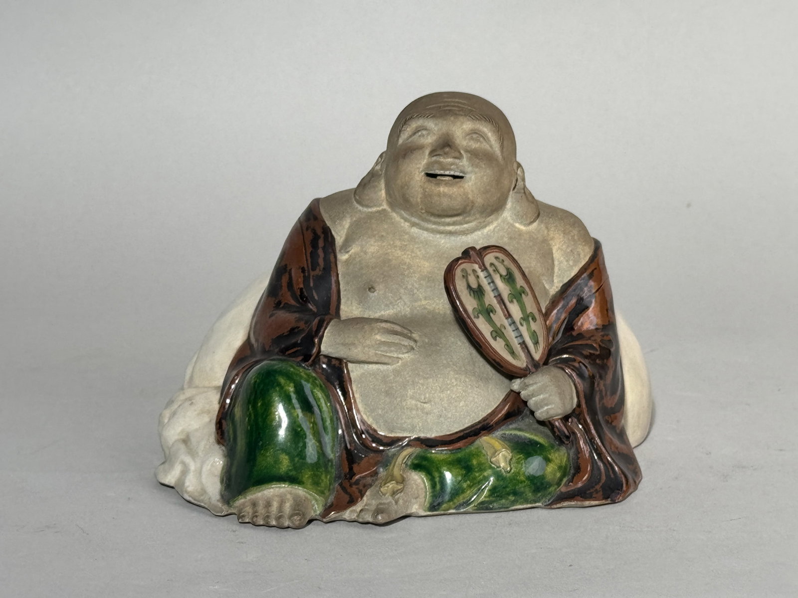 JAPANESE STUDIO POTTERY FIGURINE BY TOZAN: A Japanese Meiji period studio pottery figurine of a Hotei by Tozan, with an impressed seal at the bottom. Dimensions: Height: 4.5 in. (11.4 cm); Width: 6 in. (15.2 cm). Note: This item is in New York