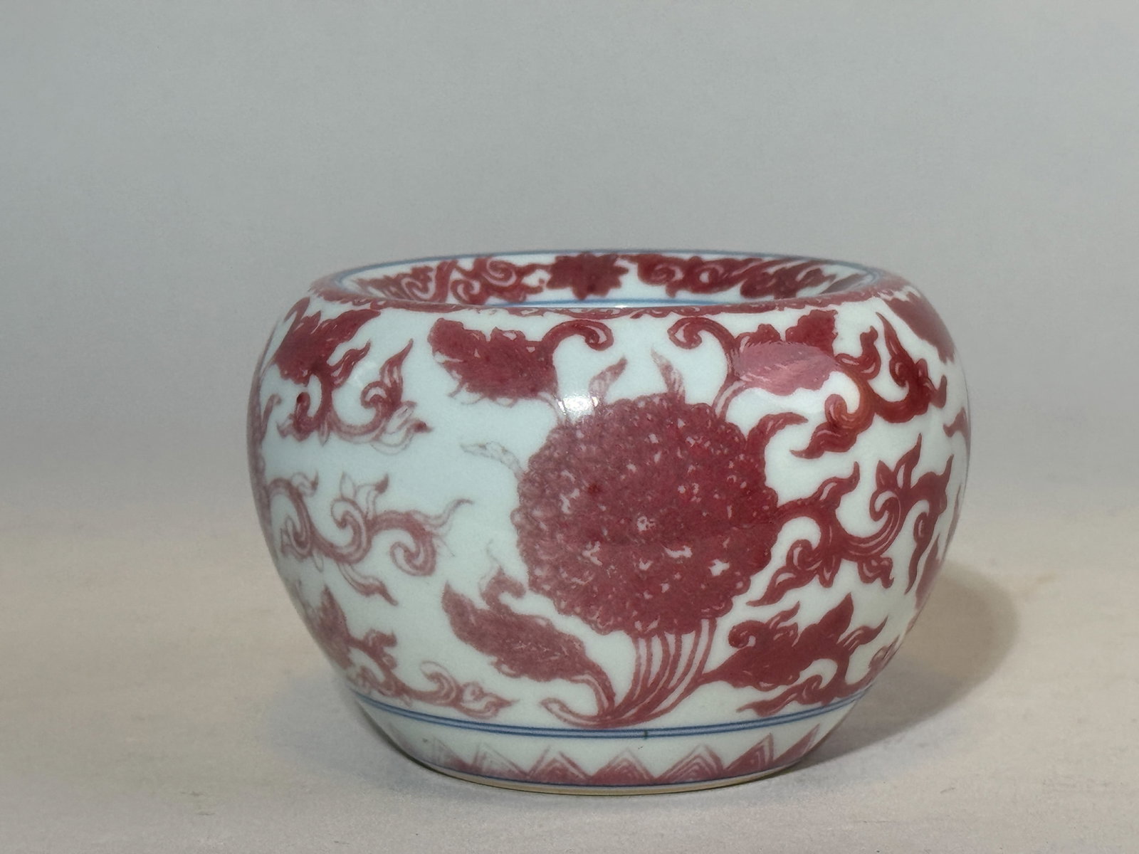 CHINESE COPPER-RED PORCELAIN SCHOLAR WATER POT: A Chinese underglaze copper-red scholar porcelain water pot with a floral motif and an underglaze blue mark at the bottom. Dimensions: Diameter: 4 in. (10.2 cm); Height: 2.75 in. (7 cm). Note: This it