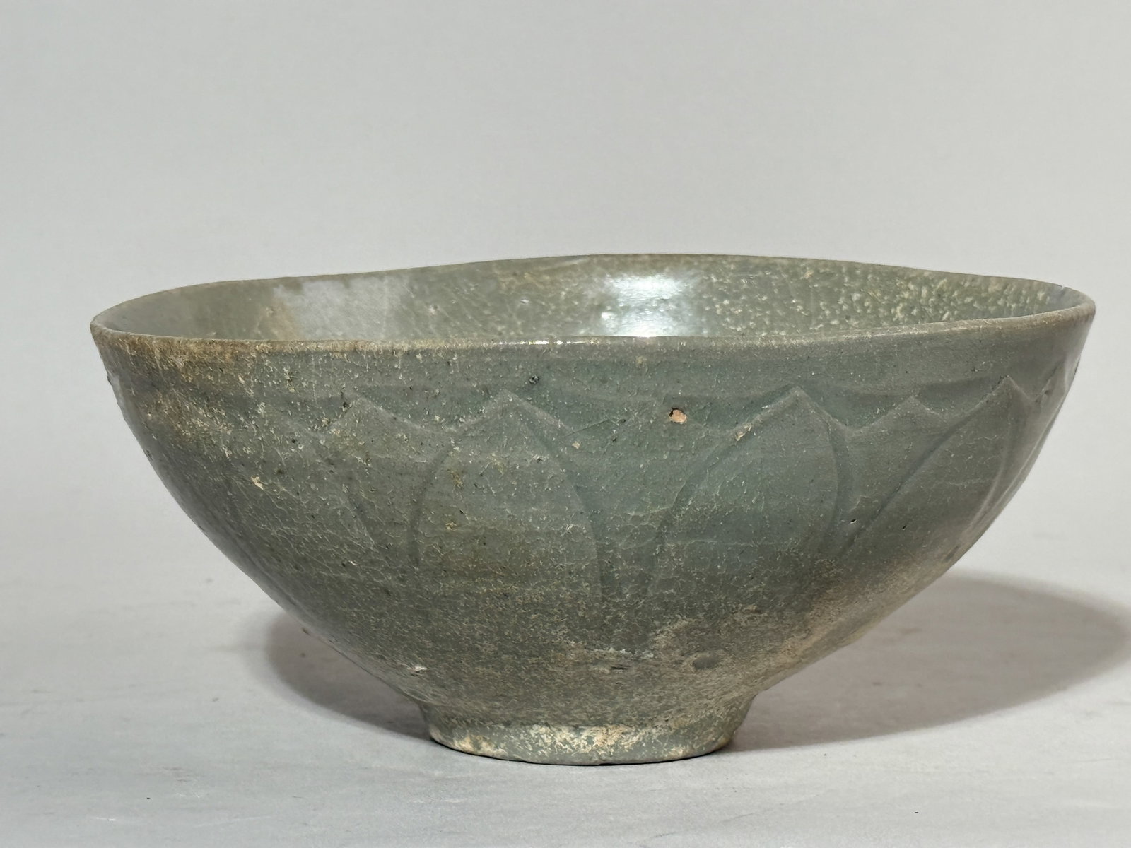 KOREAN CELADON PORCELAIN BOWL WITH LOTUS PETAL: A Korean celadon porcelain bowl with a lotus petal motif. Kiln ashes as seen in the photo, uneven rim. Dimensions: Diameter: 6.5 in. (16.5 cm); Height: 3 in. (7.6 cm). Note: This item is in New York,