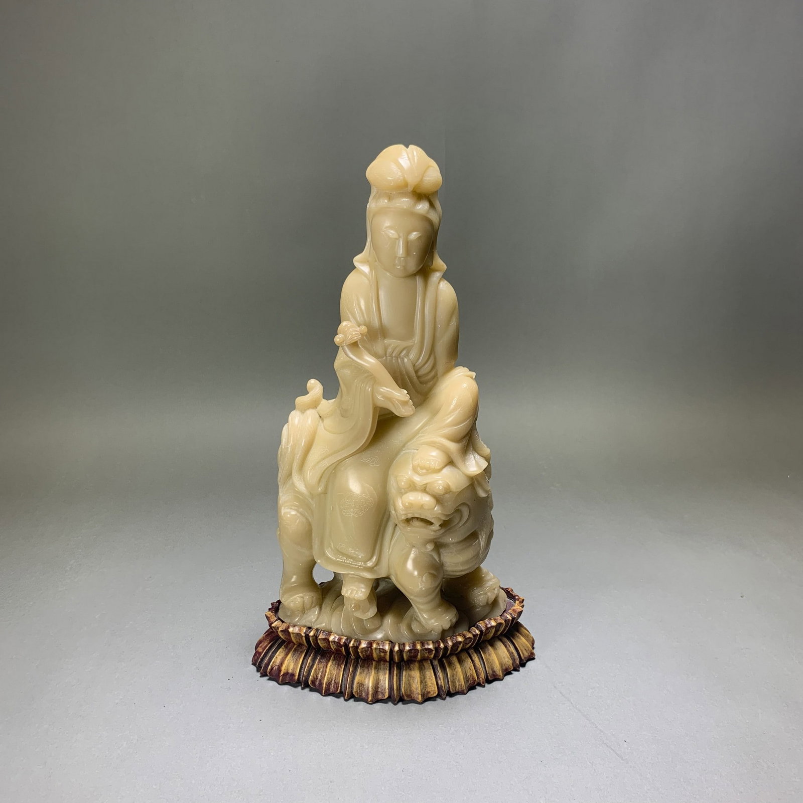 CHINESE SHOUSHAN SOAPSTONE CARVING OF GUANYIN WITH BASE: Chinese Shoushan soapstone carving of Guanyin. The figure is shown seated on a mythical beast. She is dressed in long, loose robes, holding a ruyi in the right hand. With a wooden base. 12.01"h (30.5