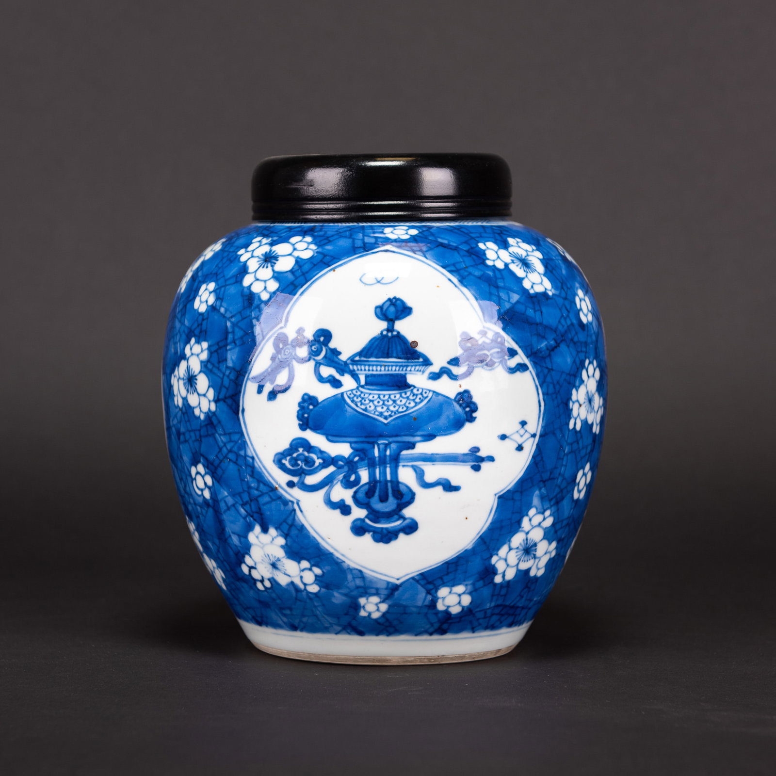 CHINESE BLUE AND WHITE "PRUNUS" JAR WITH COVER, KANGXI PERIOD: Chinese blue and white "prunus" jar with cover, decorated with three panels enclosing antique and precious objects, all reserved on a blue prunus-spray "ice-crack" ground. 8.66"h x 9.25"w (22 x 23.5