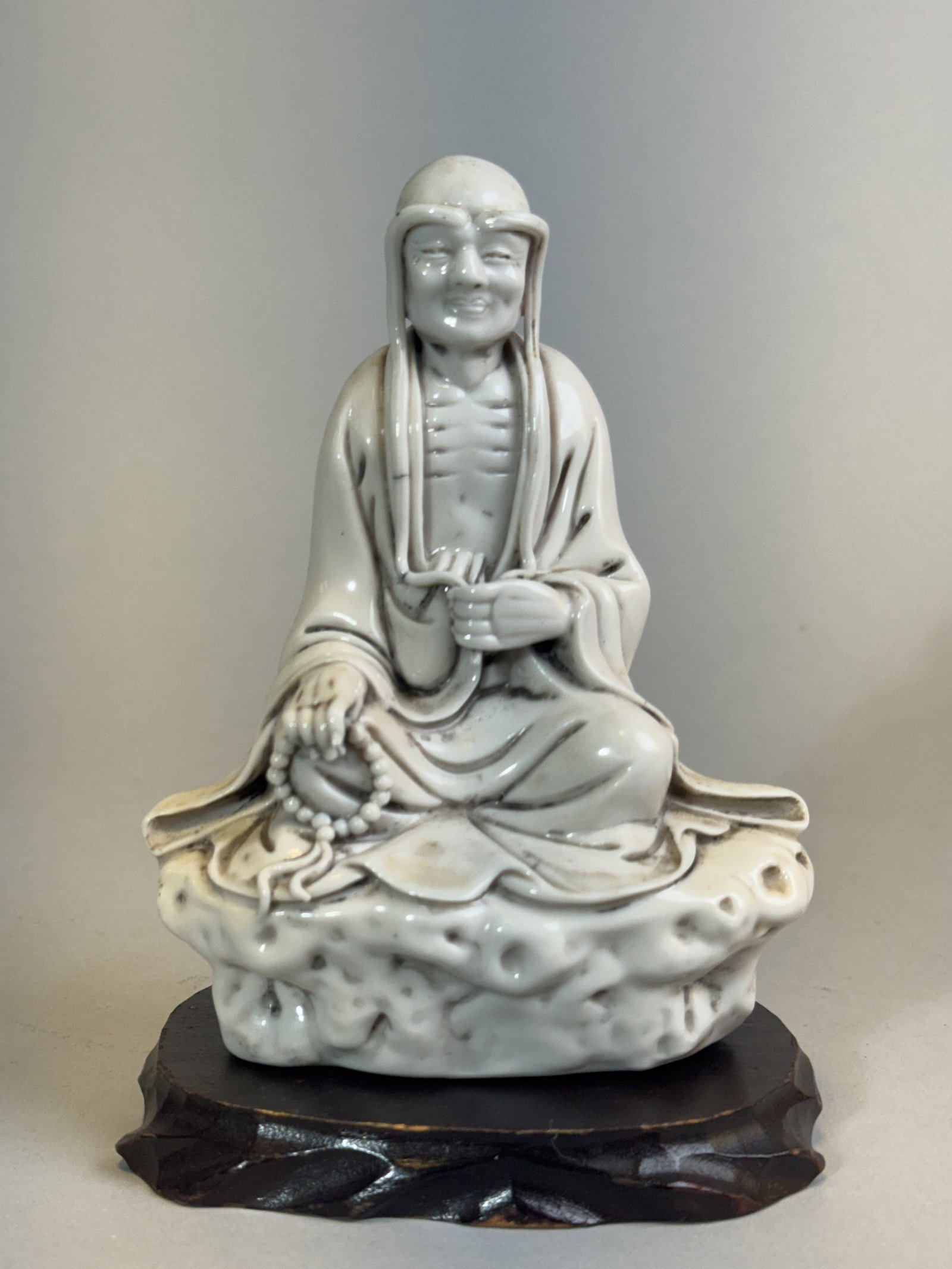 CHINESE DEHUA PORCELAIN LOHAN: Chinese Dehua porcelain lohan on a wood stand. Dimensions: Height: 5.5 in. (14.0 cm). Note: This item is in New York, where it can be shipped from.
