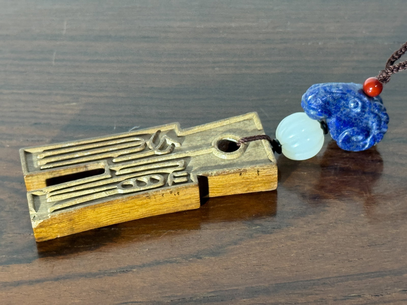 CHINESE WOOD PENDANT WITH WHITE JADE BEAD: Chinese carved wood pendant of ancient coin shape, with a white jade lobed bead and lapis ram's-head carving. Dimensions: Length: 4.5 in. (11.4 cm). Note: This item is in New York, where it can be