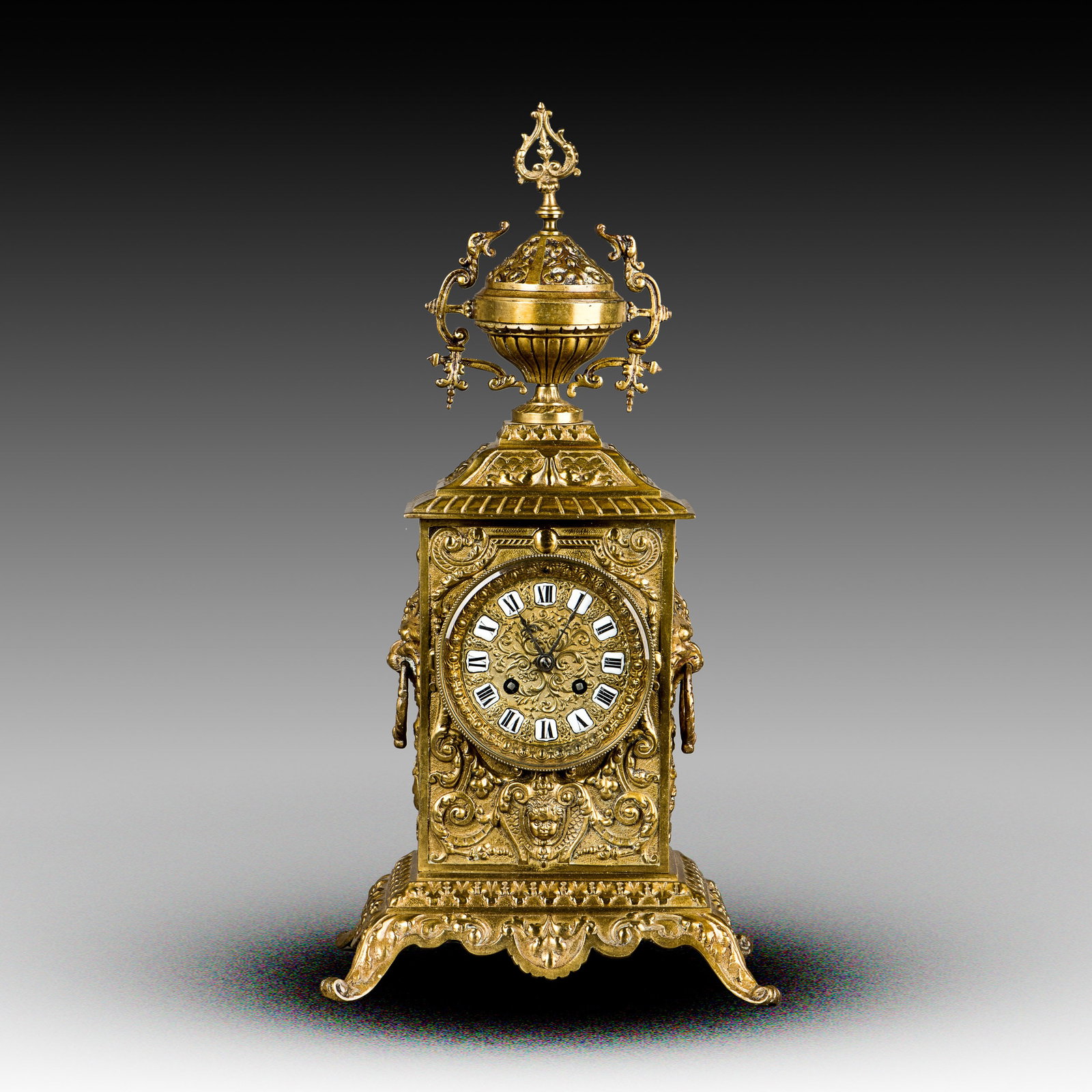 FRENCH-STYLE BRASS MANTEL CLOCK, 19TH CENTURY: 19th-century French-style brass mantel clock. Ornate cast brass case with an urn finial and animal-form ring handles on the sides, with enameled porcelain markers on the brass dial. 48"h x 25"w x 20"l