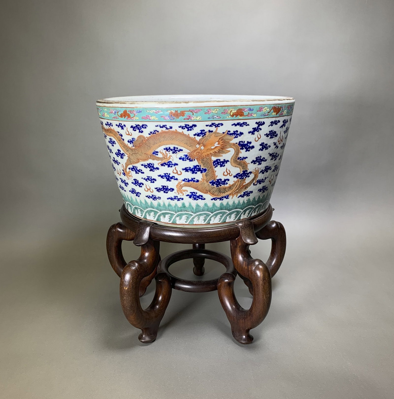 CHINESE 'DRAGON' ENAMELED JARDINIERE WITH STAND, 18TH/19TH CENTURY: Chinese 'dragon' enameled jardiniere with stand, 18th/19th century. A large polychrome enameled porcelain planter decorated with fierce four-clawed dragons chasing a flaming pearl. Comes with a rosewo