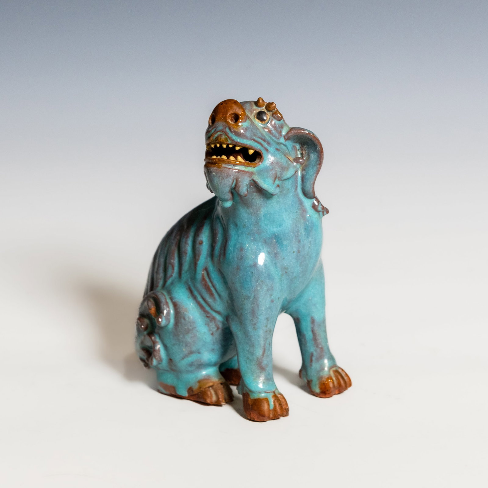 A SHIWAN TURQUOISE-GLAZED POTTERY BUDDHIST LION: A Shiwan turquoise-glazed pottery Buddhist lion, modeled seated with bared teeth and a lively expression, covered in a rich turquoise glaze with finely incised decorative details. H14.5 x 10.5 x 7 cm